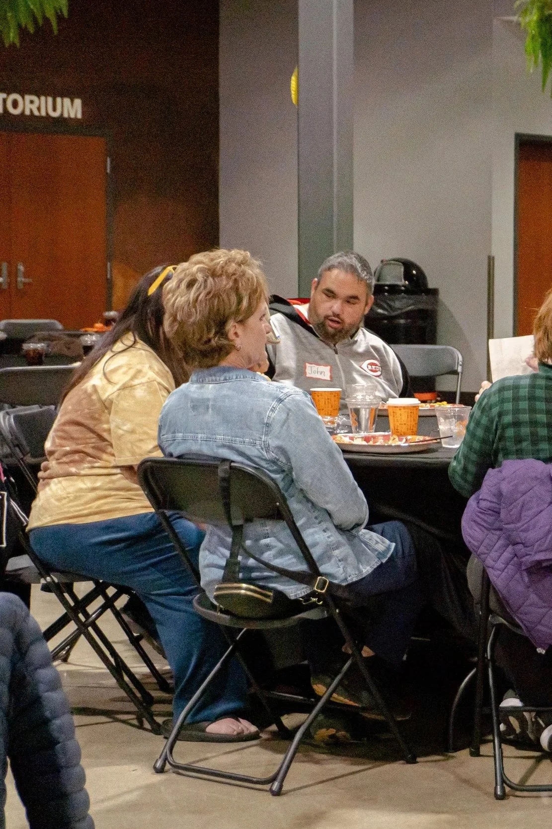 People sitting at a table having a conversation at an indoor event, with some food and drinks on the table.