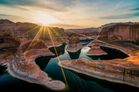 Sunset over a canyon with a winding river, showing layered rock formations and a dramatic sky.