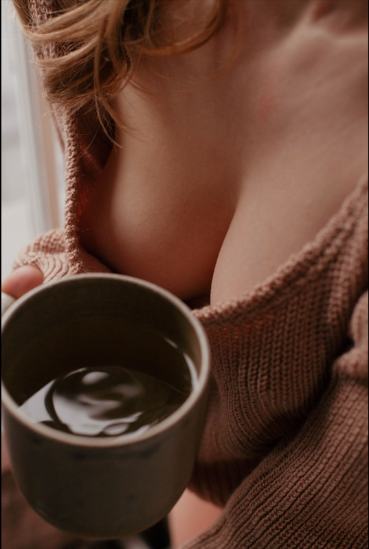 A person holding a coffee mug, with part of their upper body and a knitted sweater visible.