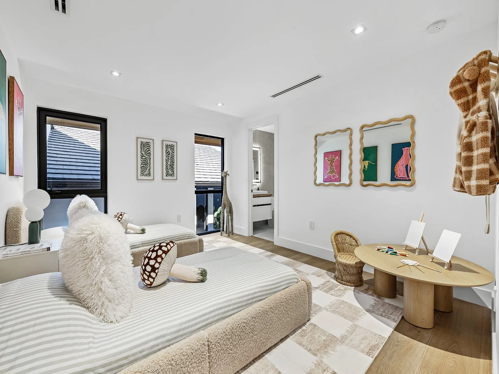 A brightly lit children's bedroom with two beds, a small table with art supplies, and decorative animals and colorful animal artwork on the walls.
