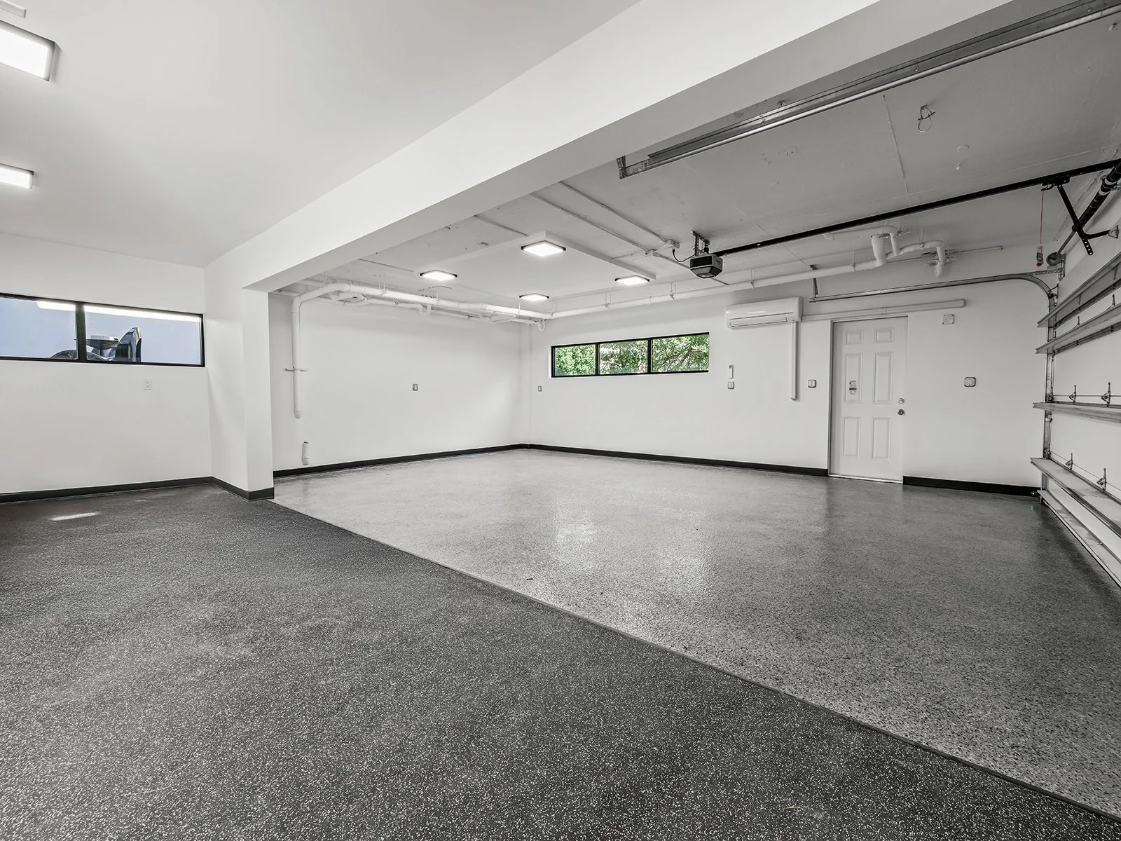 Empty two-car garage with white walls, black trim, black-speckled epoxy floor, windows, and a garage door on the right side.
