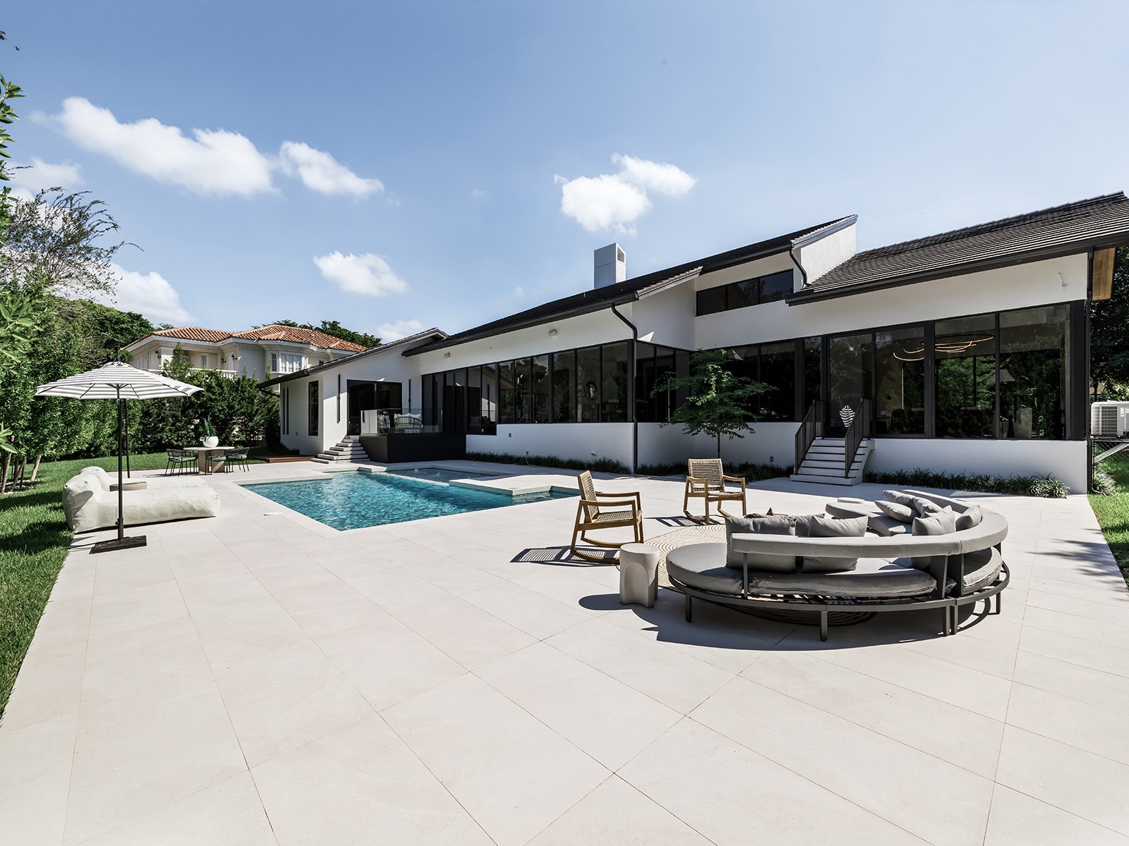 Modern backyard with swimming pool, outdoor seating, and patio area in front of a contemporary house.