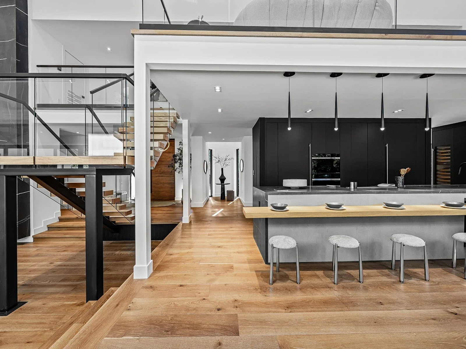 Modern open-plan kitchen and living space with wooden flooring, black cabinets, and sleek black pendant lights.