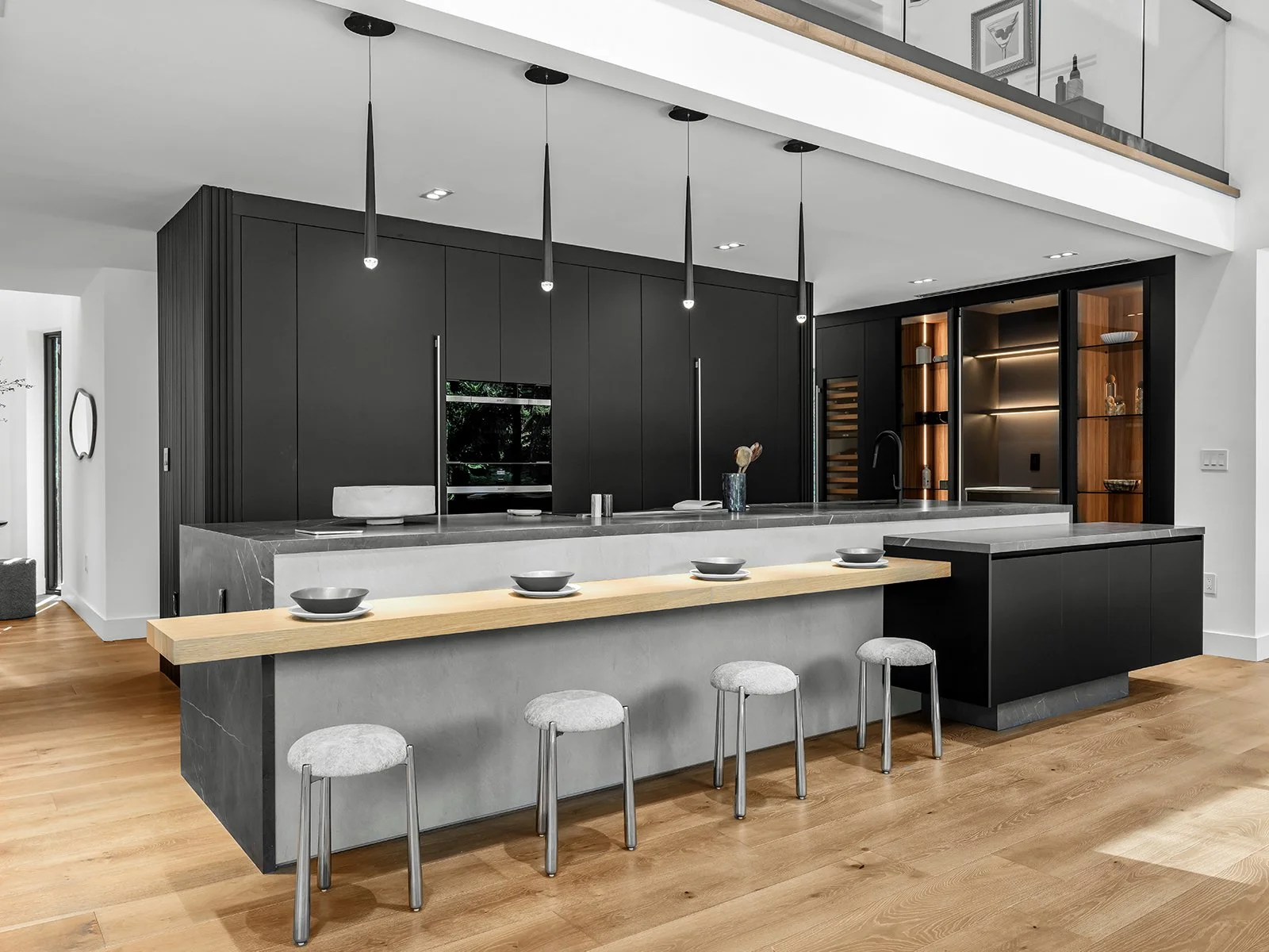 Modern kitchen with black cabinets, a spacious black and gray island, and a built-in wooden shelving unit, with a light wood floor and minimalist decor.