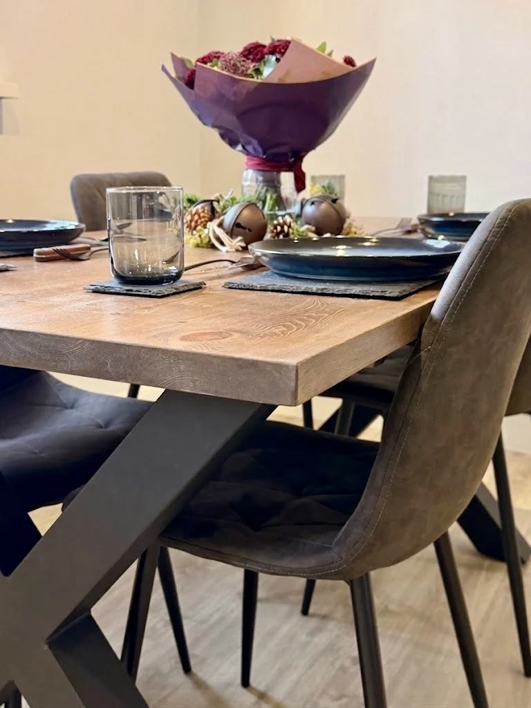 Dining table set with black plates, glasses, a bouquet of flowers, and decorative ornaments in the background.
