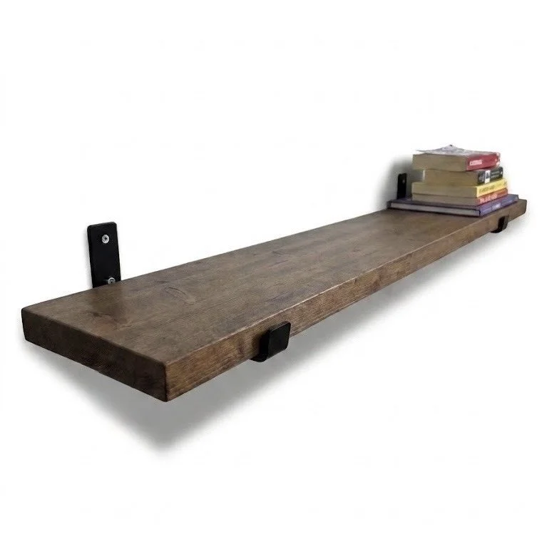 A wooden floating shelf with black metal brackets holding it on a white wall, with a small stack of books on the right side.