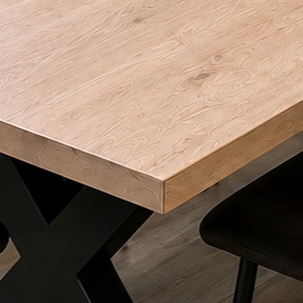Close-up of a light-colored wooden table with black metal legs in a room with wooden flooring