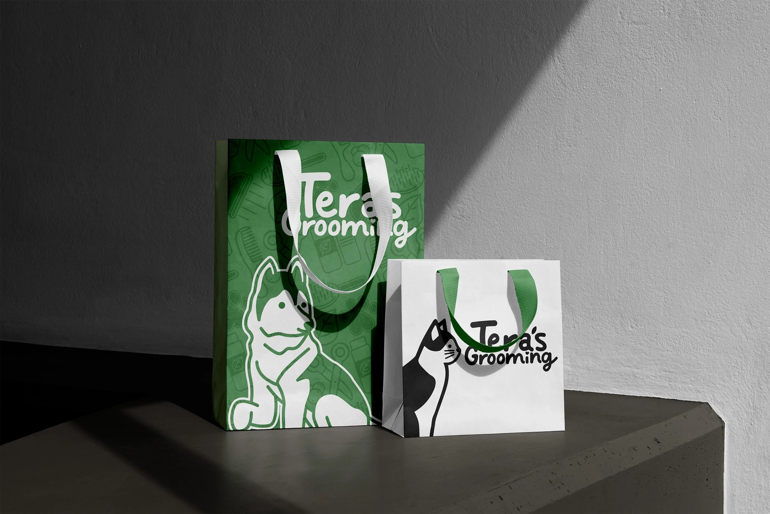 Two shopping bags with pet grooming branding, one green with a dog illustration, and one white with a cat illustration, placed on a dark surface next to a textured white wall.