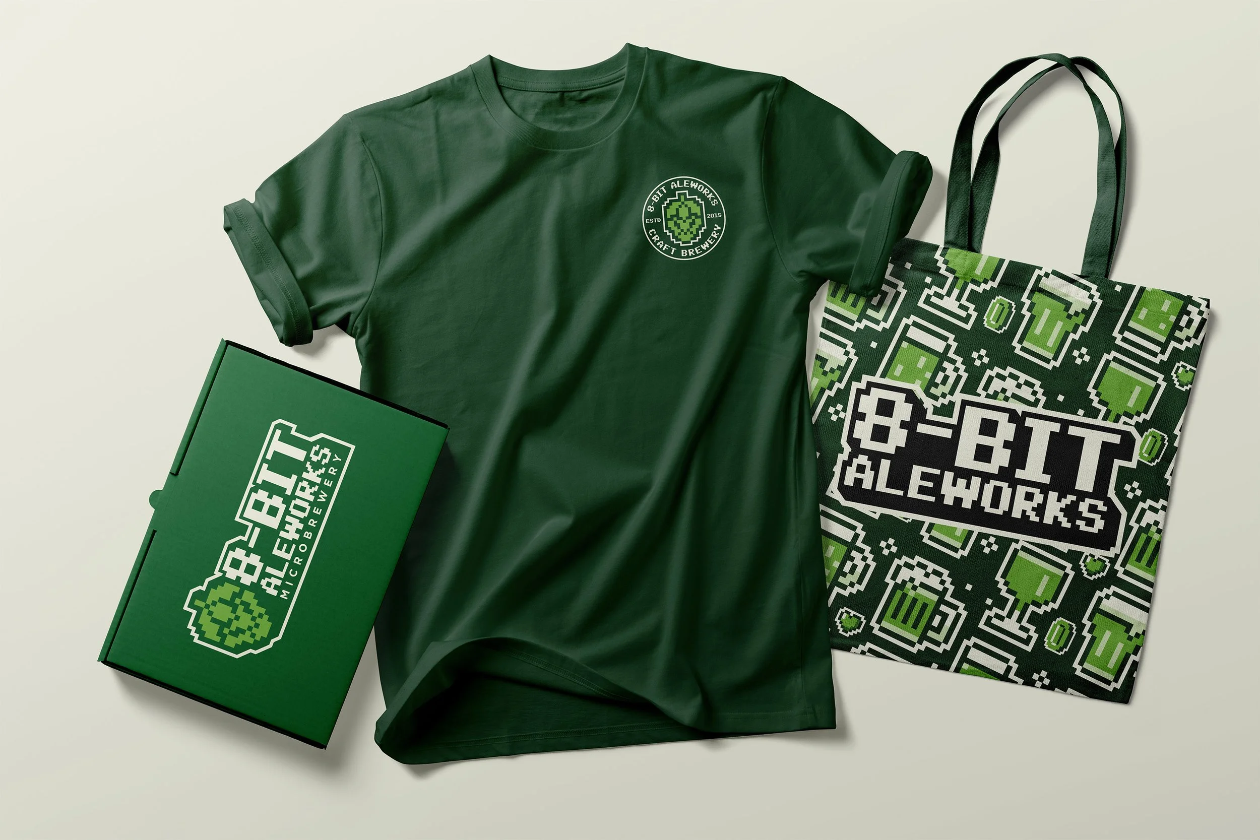 Green T-shirt with '8-BIT ALEWORKS CRAFT BREWERY' logo, a green box with similar branding, and a tote bag with pixelated graphics and the same branding.
