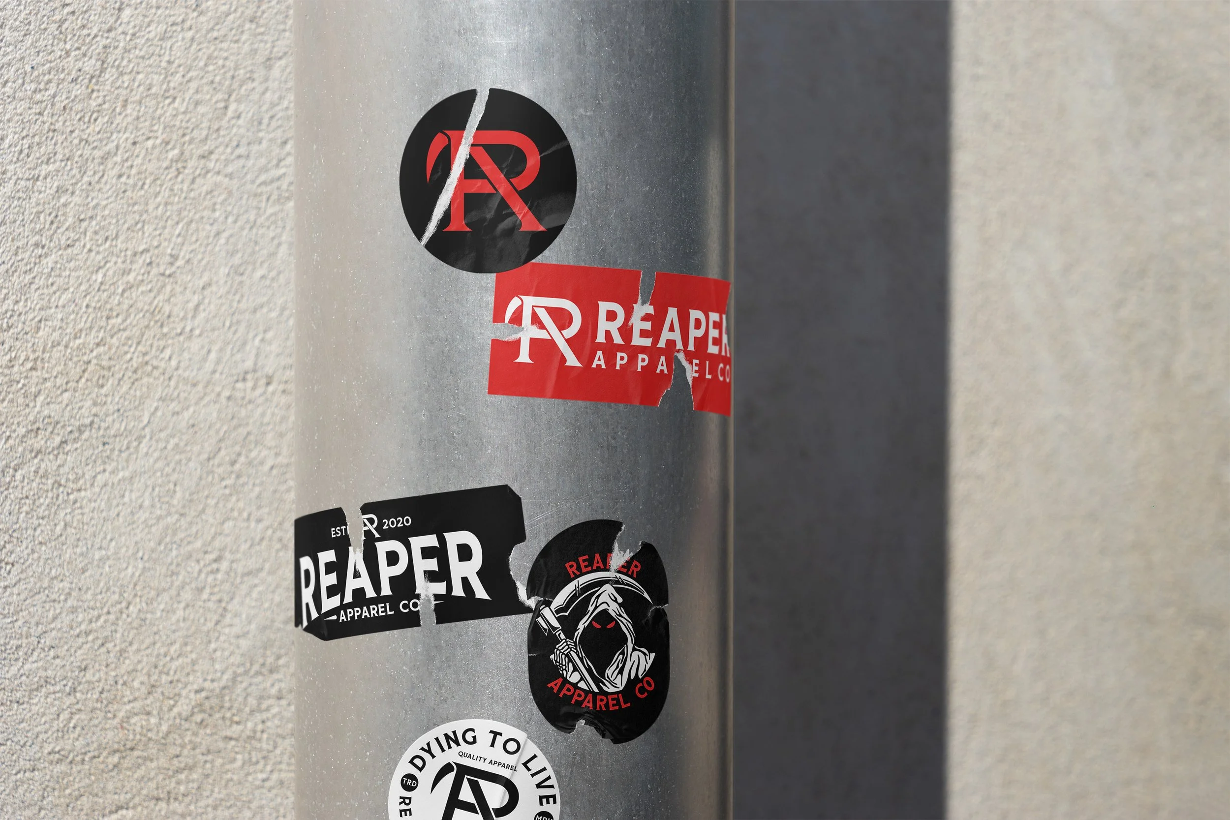 A metallic pole with various Reaper Apparel stickers adhered to it, including a red and black logo, and a sticker featuring a hooded figure with red eyes holding a scythe.