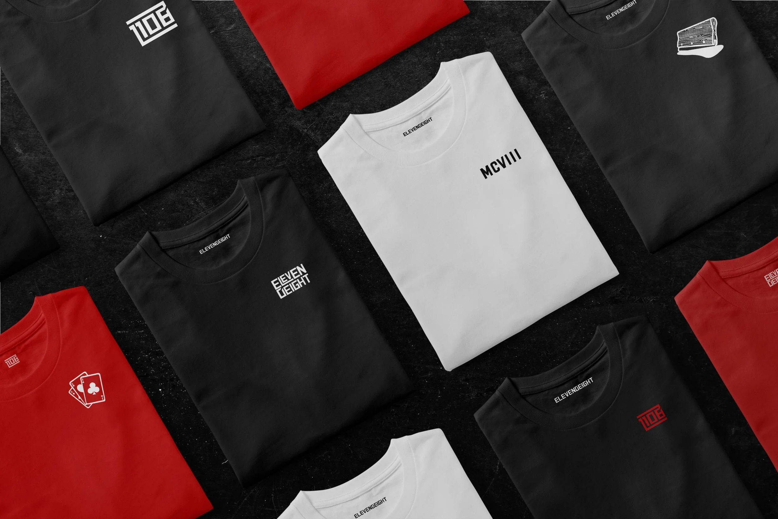 Various folded T-shirts in red, black, and white with logos and text, arranged on a dark surface.