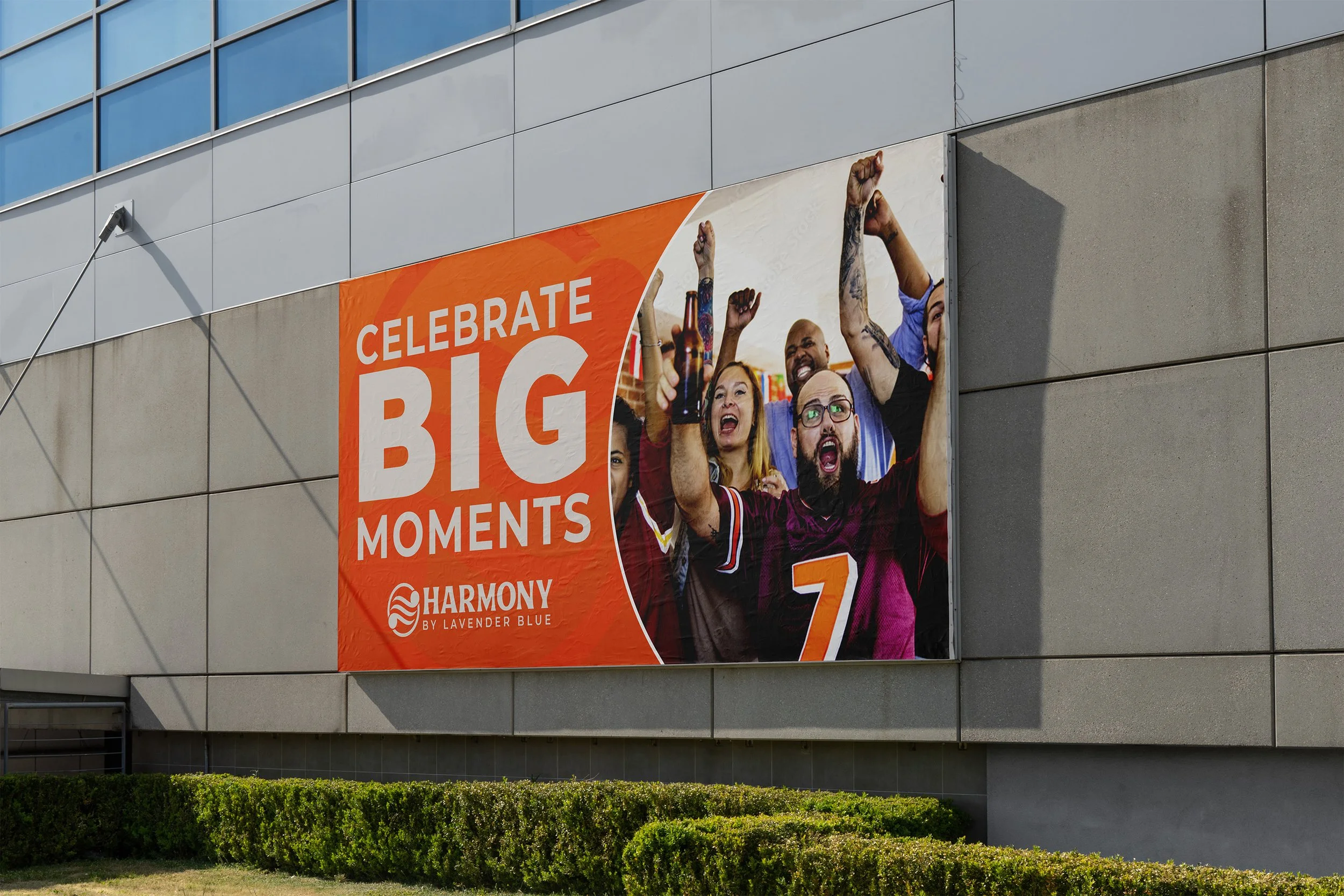 A large outdoor banner on a building with the text 'Celebrate Big Moments' and a group of diverse people cheering and celebrating, some holding drinks, at a social gathering or party.