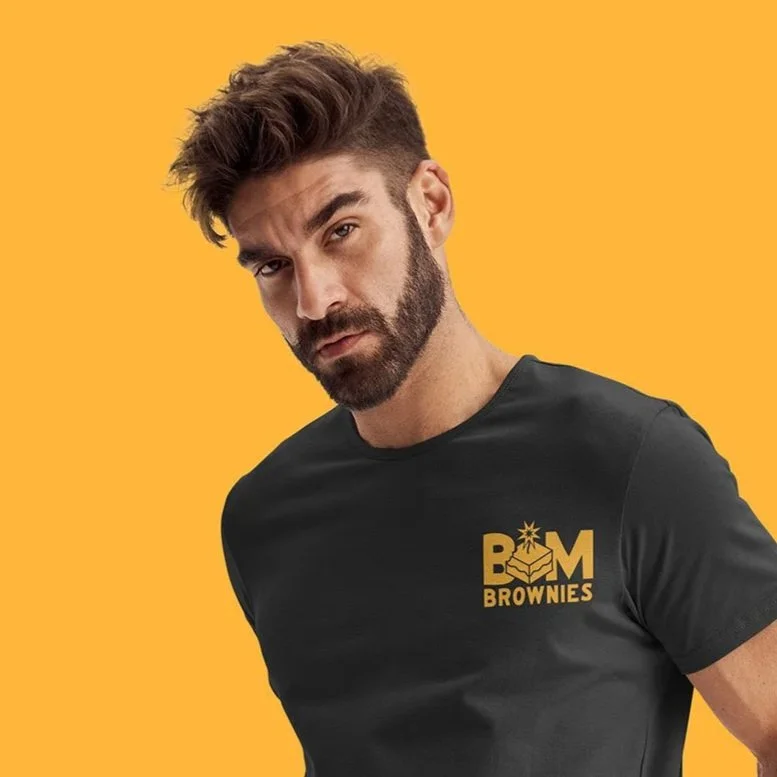 A man with a beard and styled hair wearing a black t-shirt with a gold logo that reads 'B&M Brownies' on an orange background.