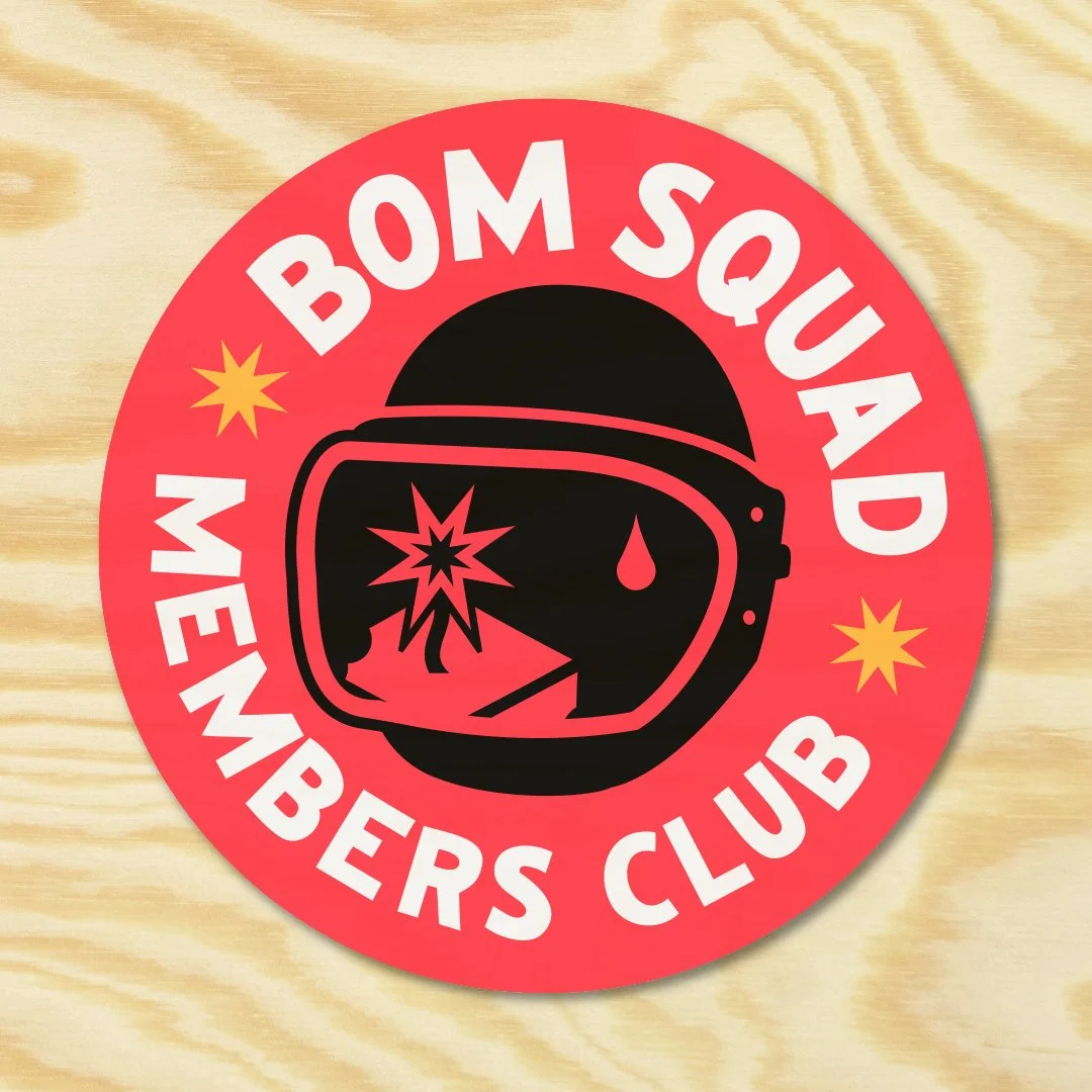 A circular sticker with a red background, featuring a black helmet and goggles with a bullet hole, a drop of blood, and an explosion inside the goggles. The text around the circle reads 'BOM SQUAD MEMBERS CLUB' in white letters, with yellow starburst