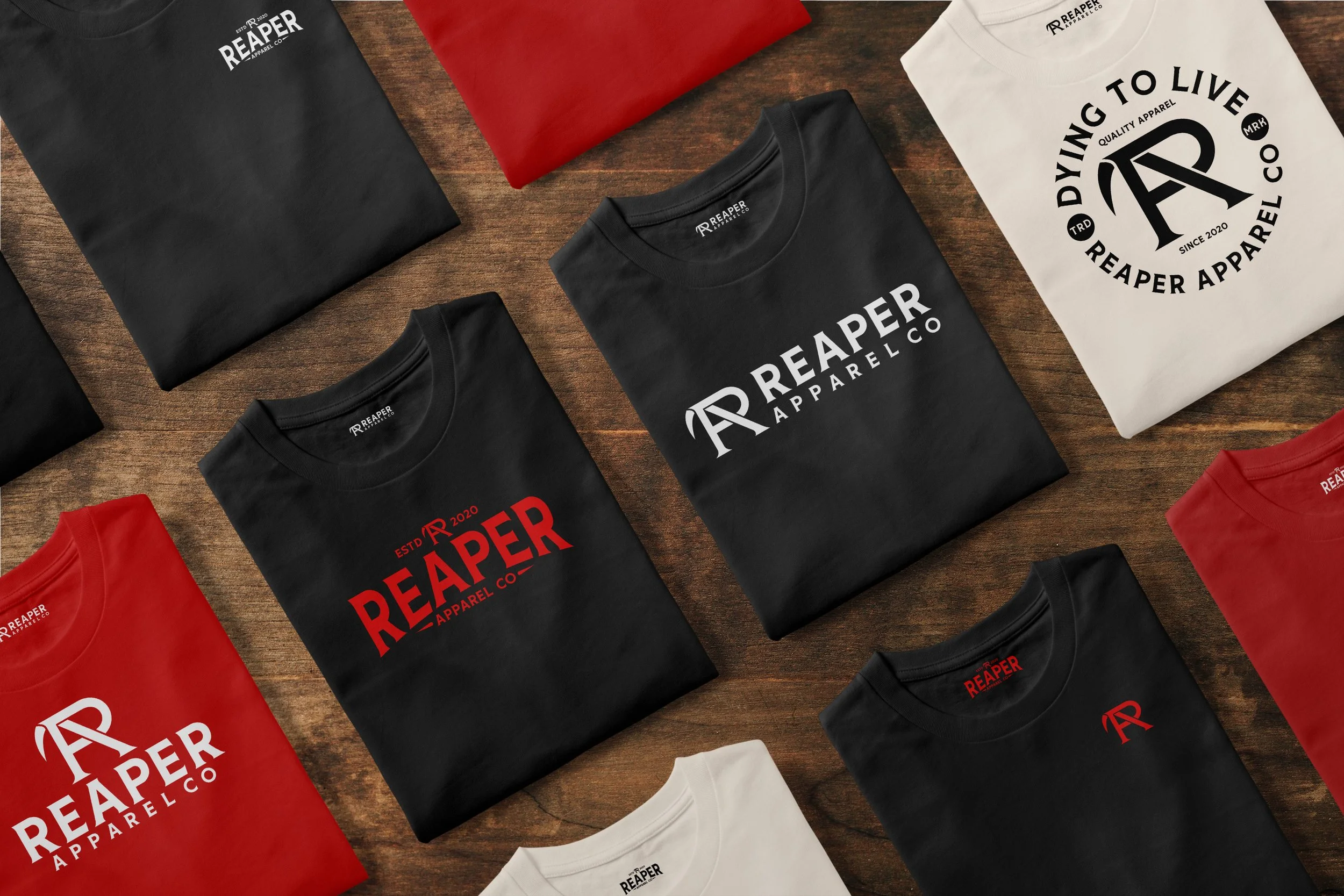 Multiple folded T-shirts on a wooden surface, with branding and logos for Reaper Apparel Co in black, white, and red.