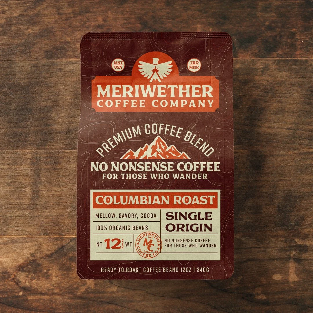Coffee bag labeled Meriwether Coffee Company Columbian Roast, with mountain graphic, indicating premium single-origin coffee, 12 ounces, made from organic beans.