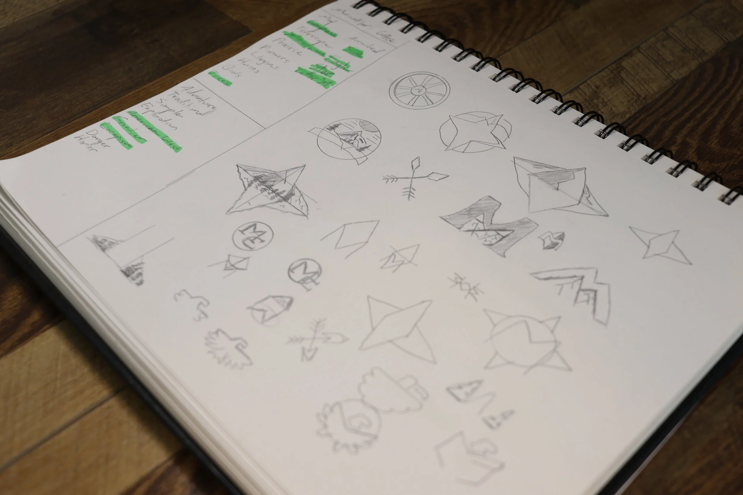 Open sketchbook with sketches of geometric shapes, arrows, and decorative elements on a wooden table.