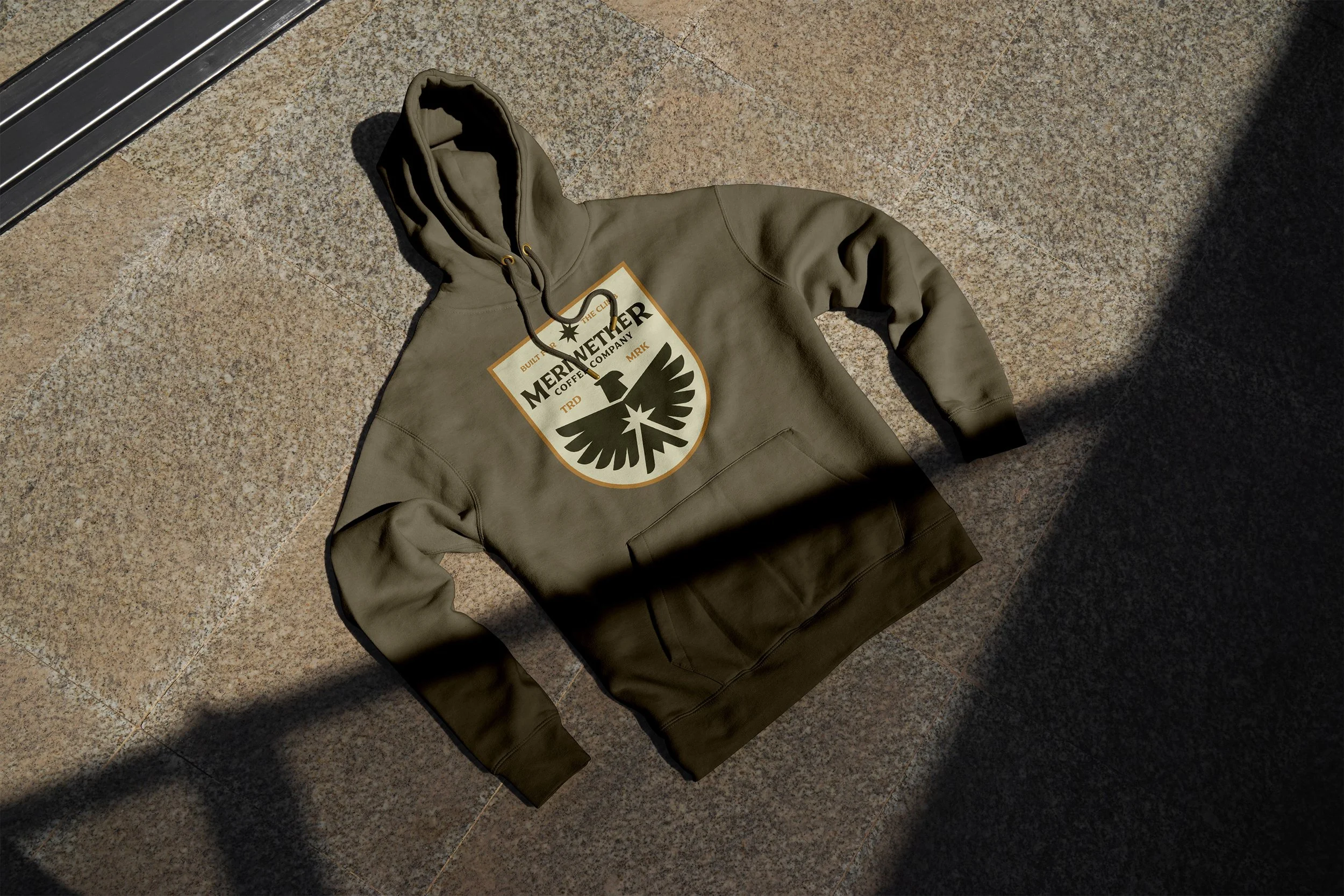 Green hoodie with a graphic logo on the front, lying on a tiled surface.