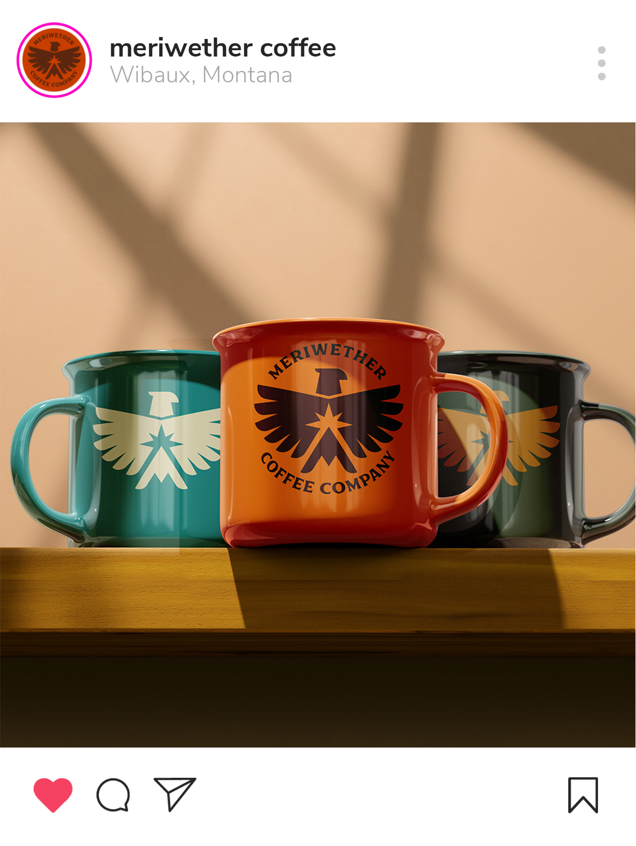 Three colorful mugs with the Meriwether Coffee Company logo, placed on a wooden surface with shadowed background.