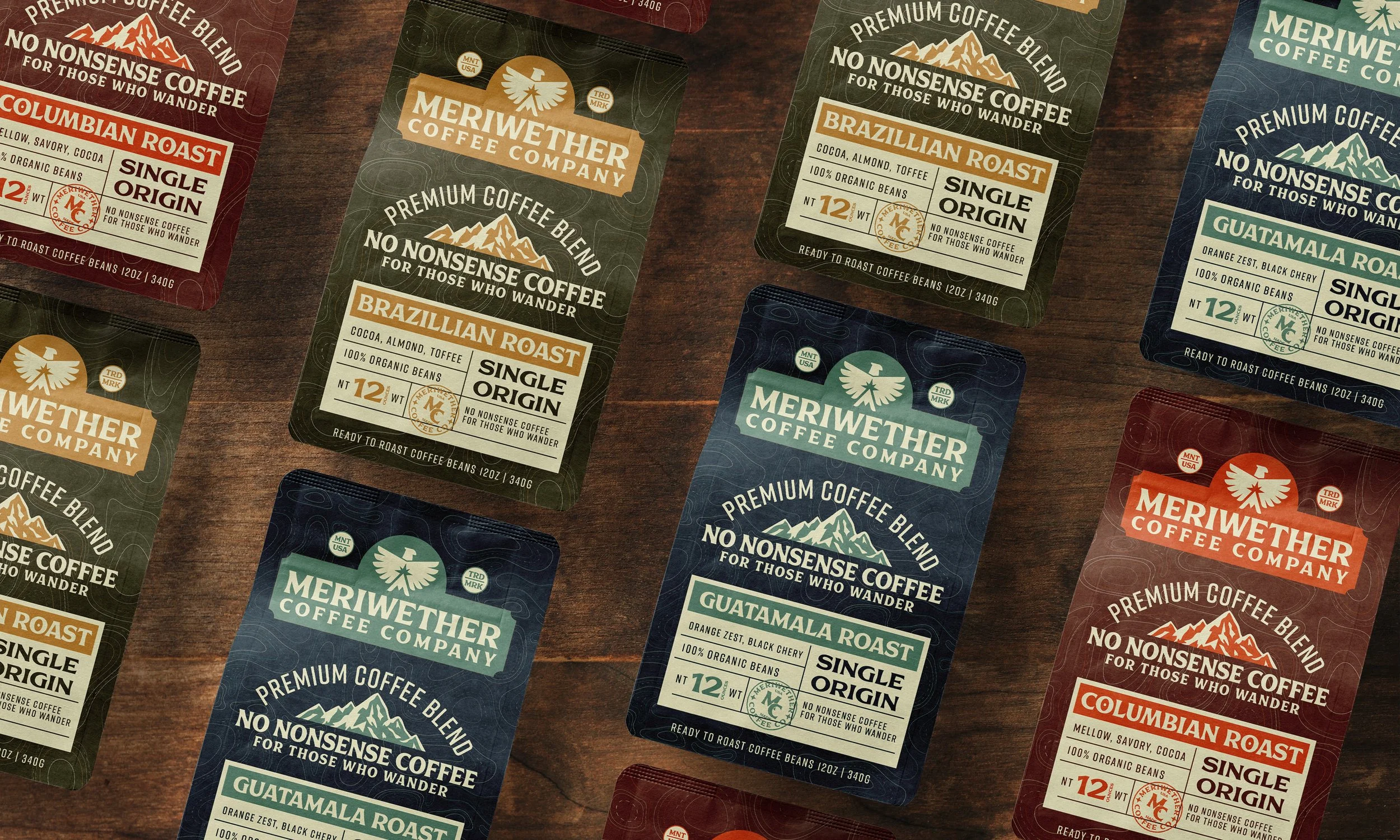 Multiple packets of Meriwether Coffee Company premium coffee blends spread out on a wooden surface, featuring flavors such as Columbian Roast, Braziilian Roast, and Guatemala Roast, with labels indicating single origin, 12 ounces, and organic beans.