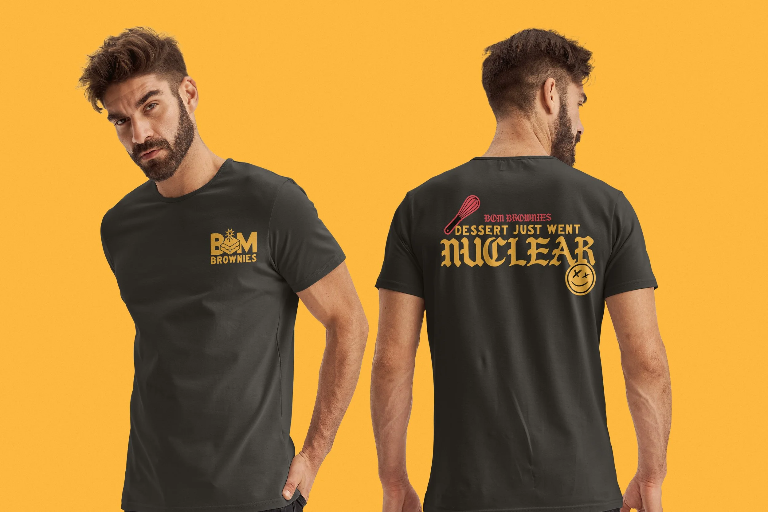Two men with beards and styled hair wearing black t-shirts with graphic prints, standing against a solid yellow background. One man faces forward with a serious expression, while the other faces away, showing the back of his shirt with larger graphic