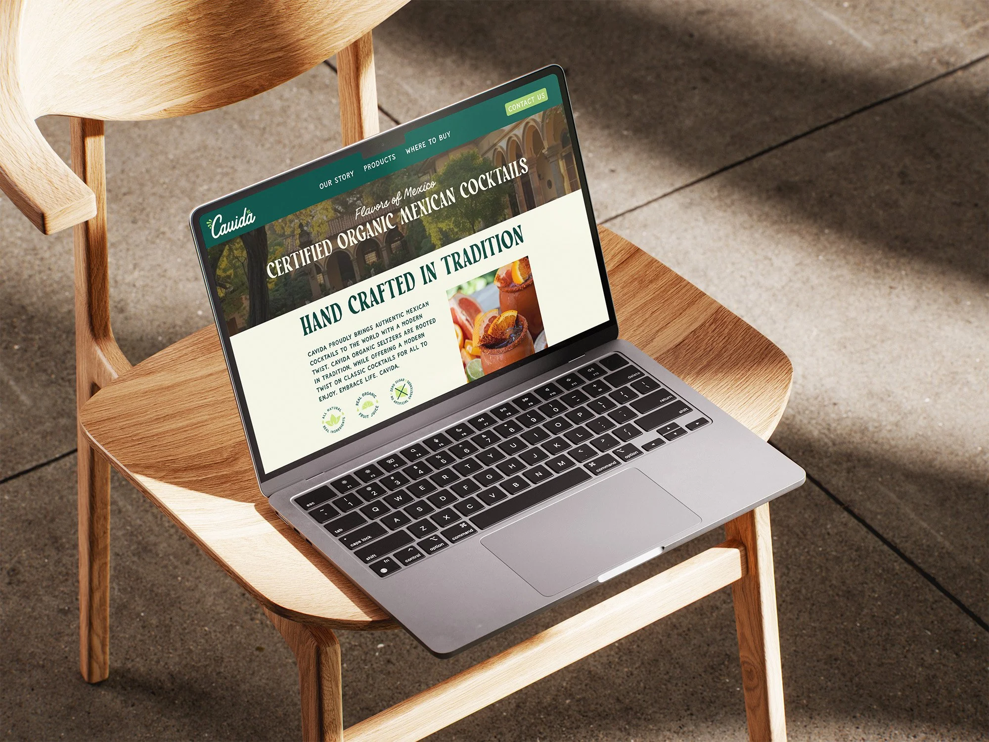 A silver laptop on a wooden chair displaying a website about organic Mexican cocktails.