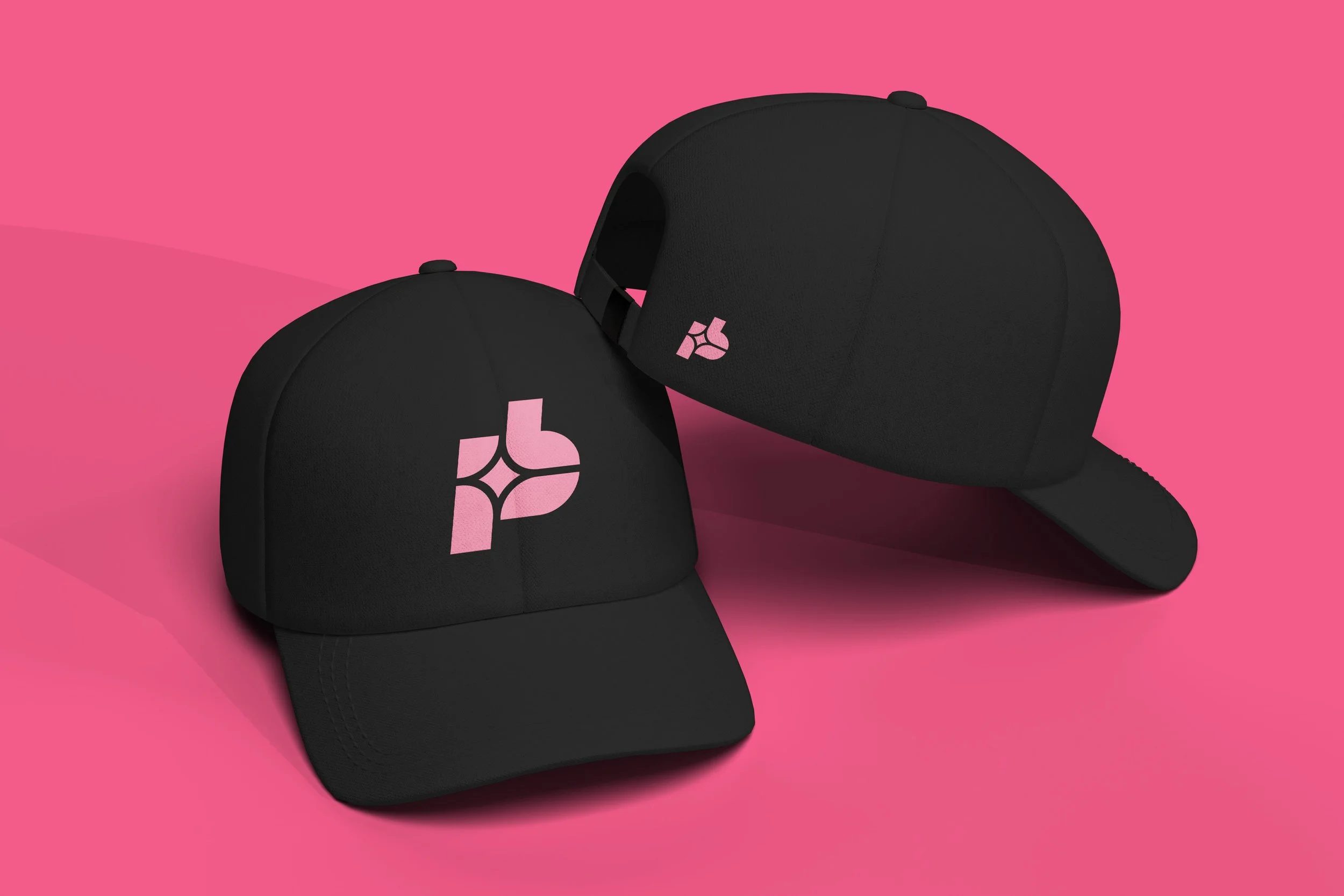 Two black baseball caps with pink logos on a pink background.