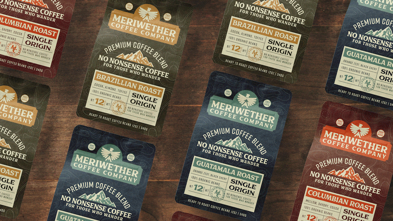 Assorted bags of Meriwether Coffee Company specialty coffee beans on a wooden surface, featuring different flavors such as Brazilian Roast, Guatamala Roast, and Columbian Roast, each with unique packaging colors and labels.