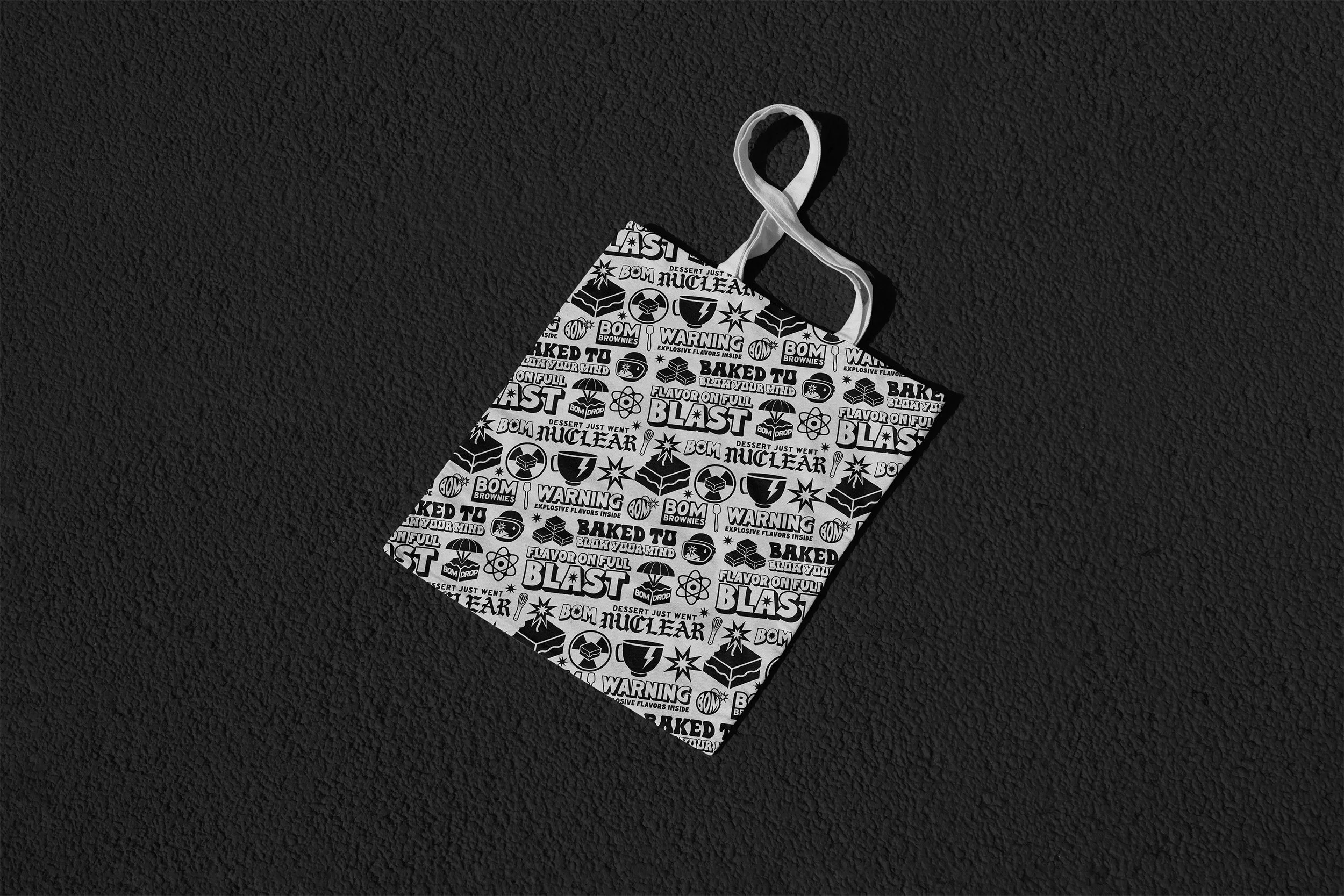 A black and white patterned baggage tag on a textured black surface. The pattern includes words and symbols related to explosive flavors and warnings, with phrases like "Baked to Blast," "Flavor on Full Blast," and "Warning," along with icons of atomic symbols, explosions, and bombs.