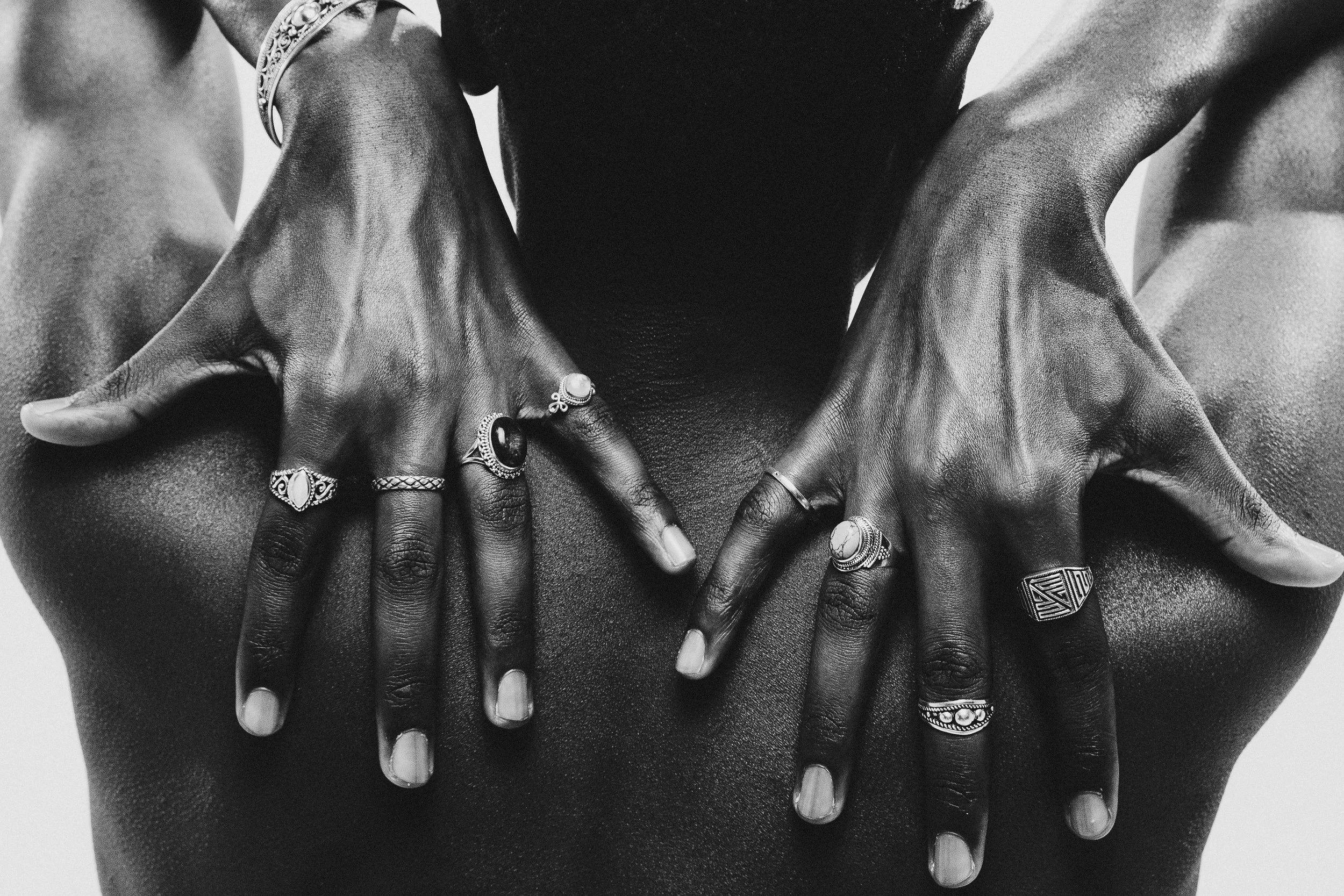 A black and white photo of a person's hands with multiple rings, placed on their bare chest, with the person's face not visible.