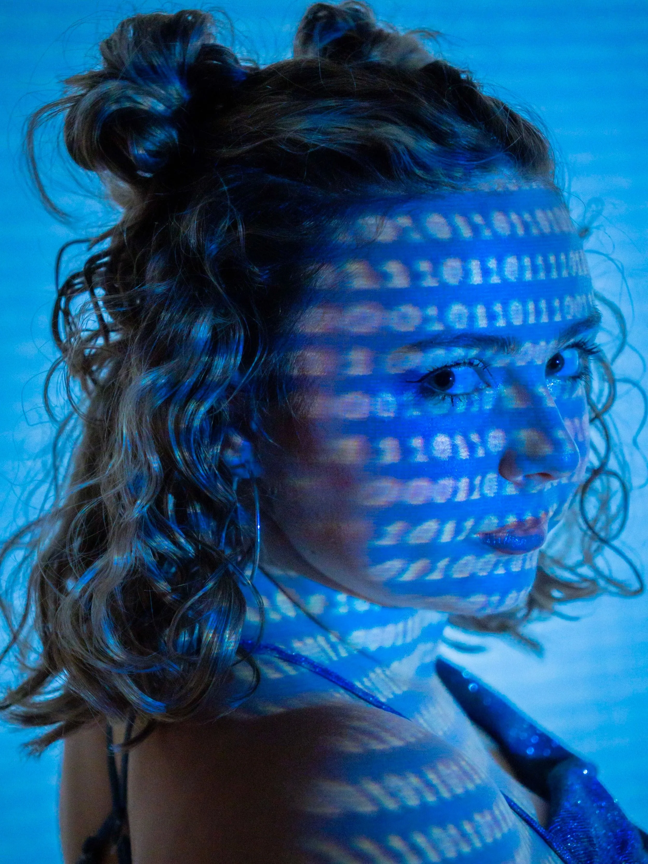 A woman with curly hair illuminated by blue light and code projection on her face.