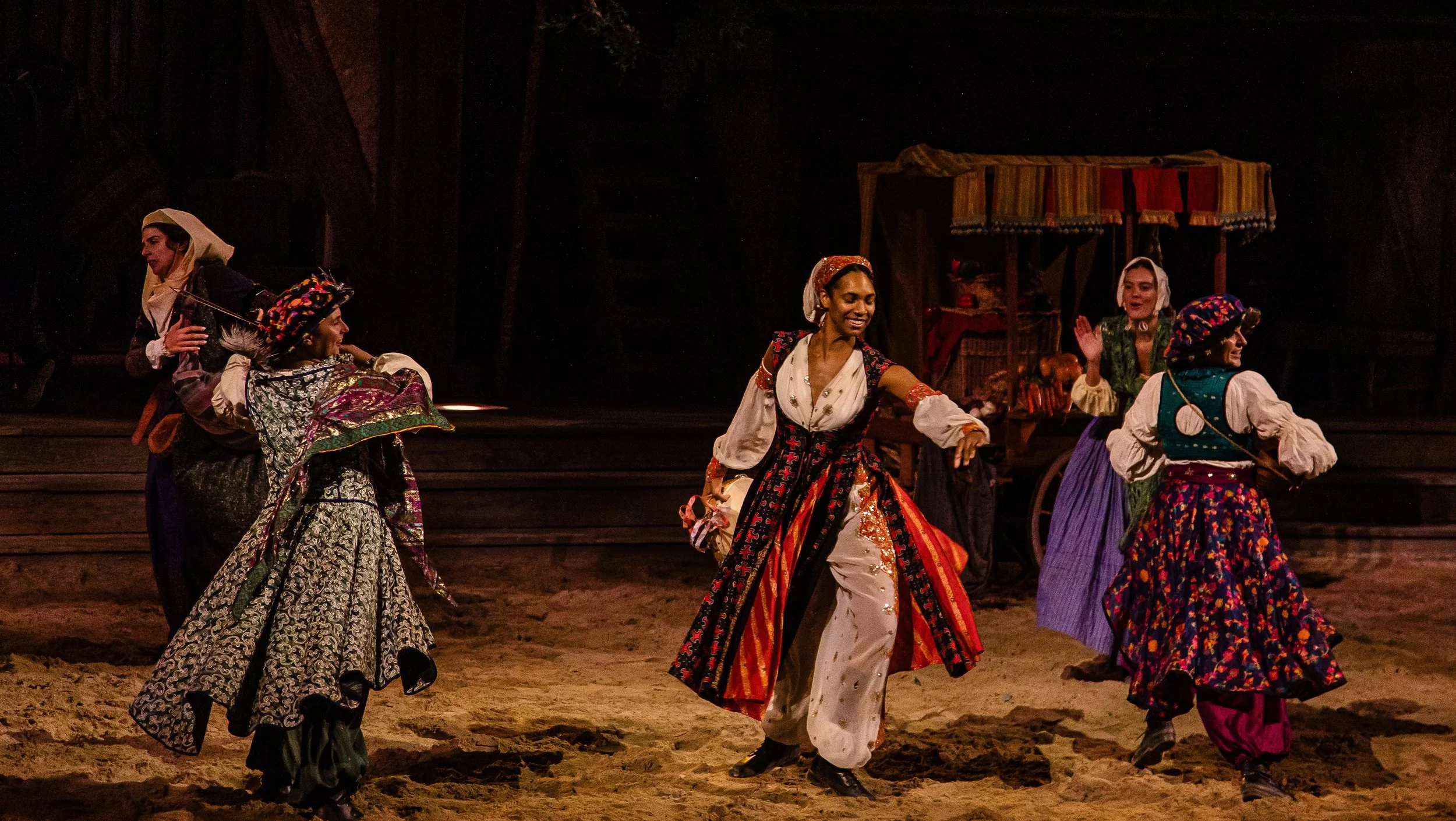 Performers in colorful traditional costumes dancing on stage during a theatrical show.