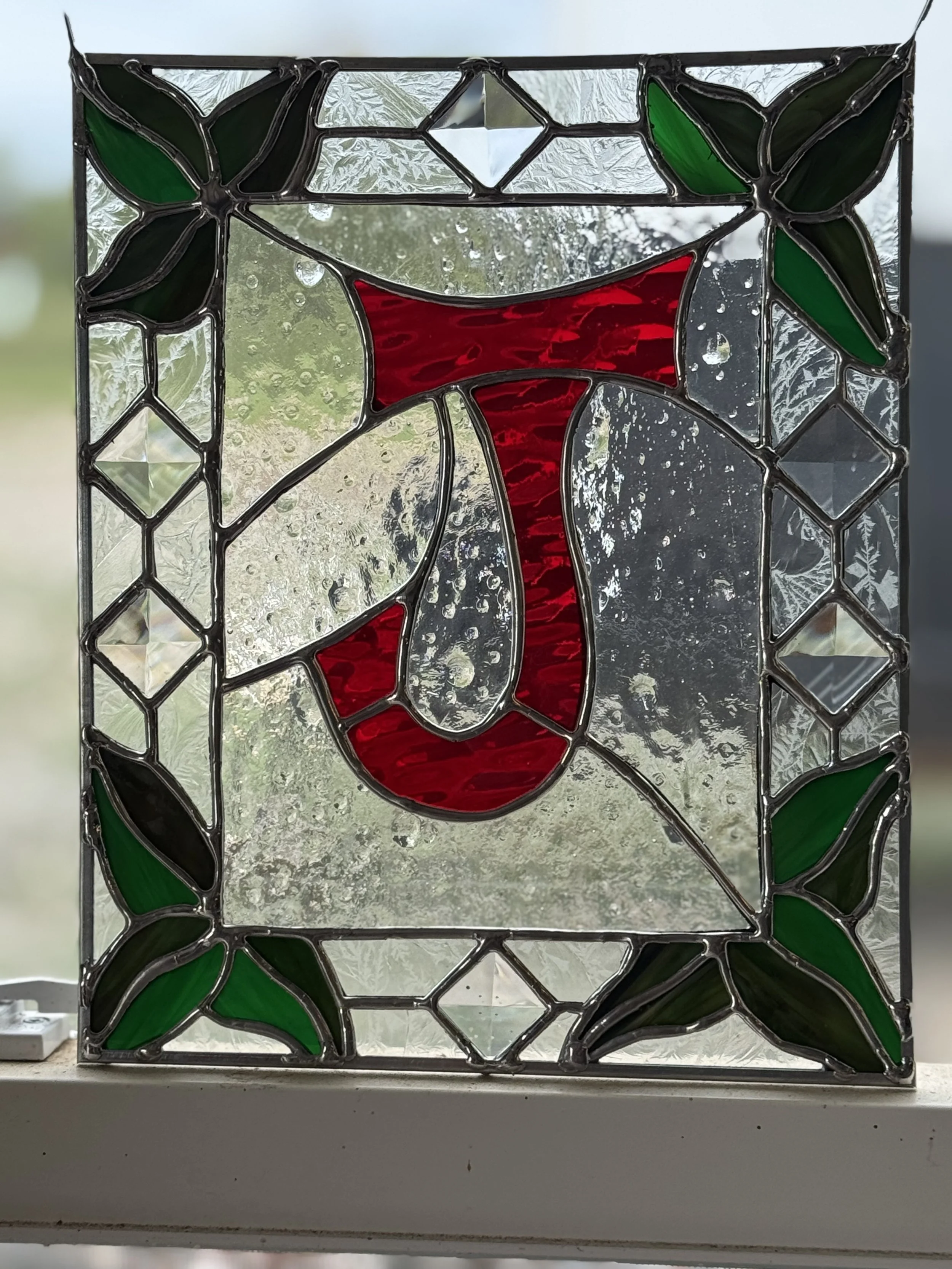 A stained glass window depicting a red flower with green leaves.
