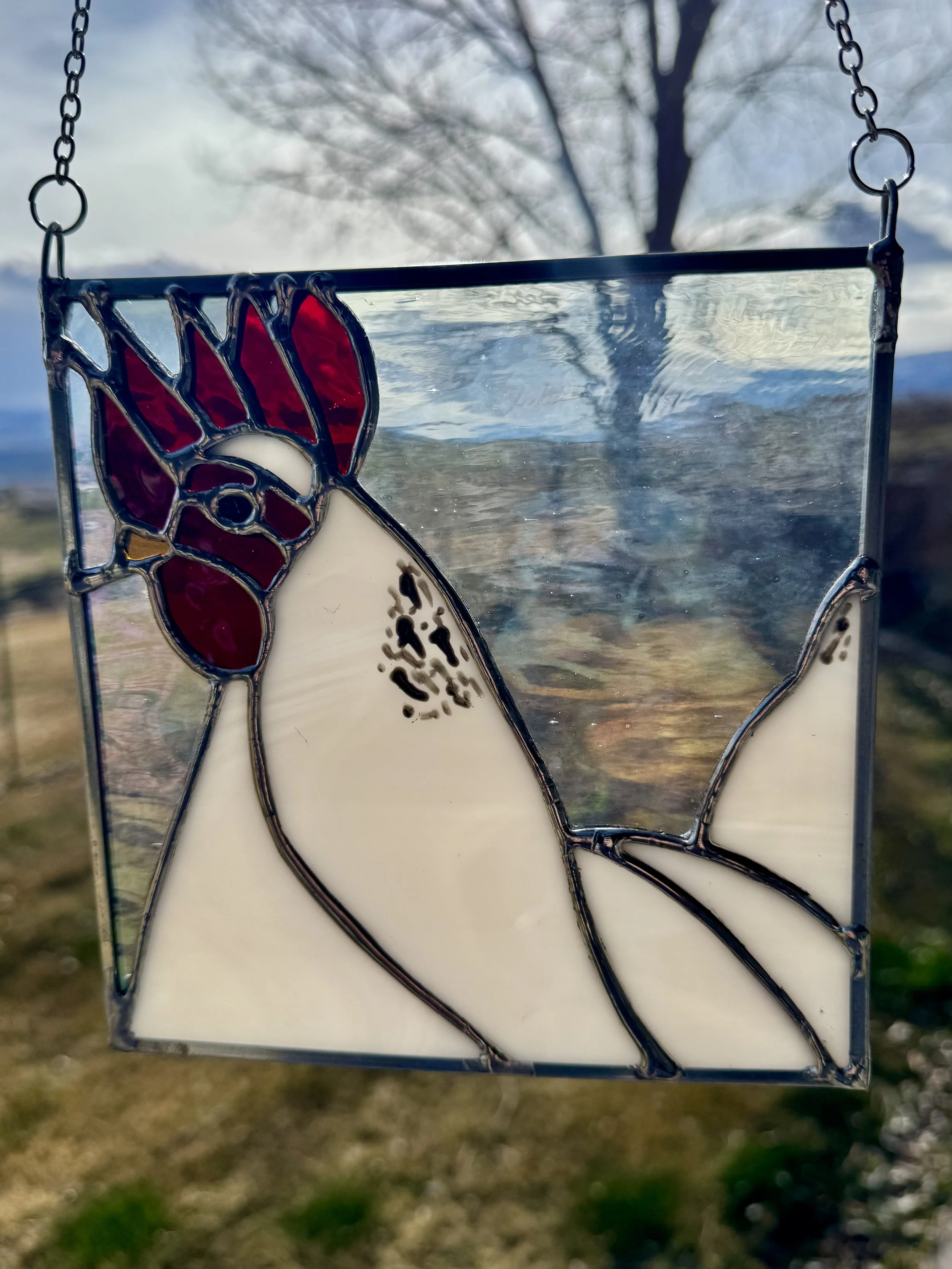 A stained glass ornament hanging outdoors with a background of a bare tree and sky.