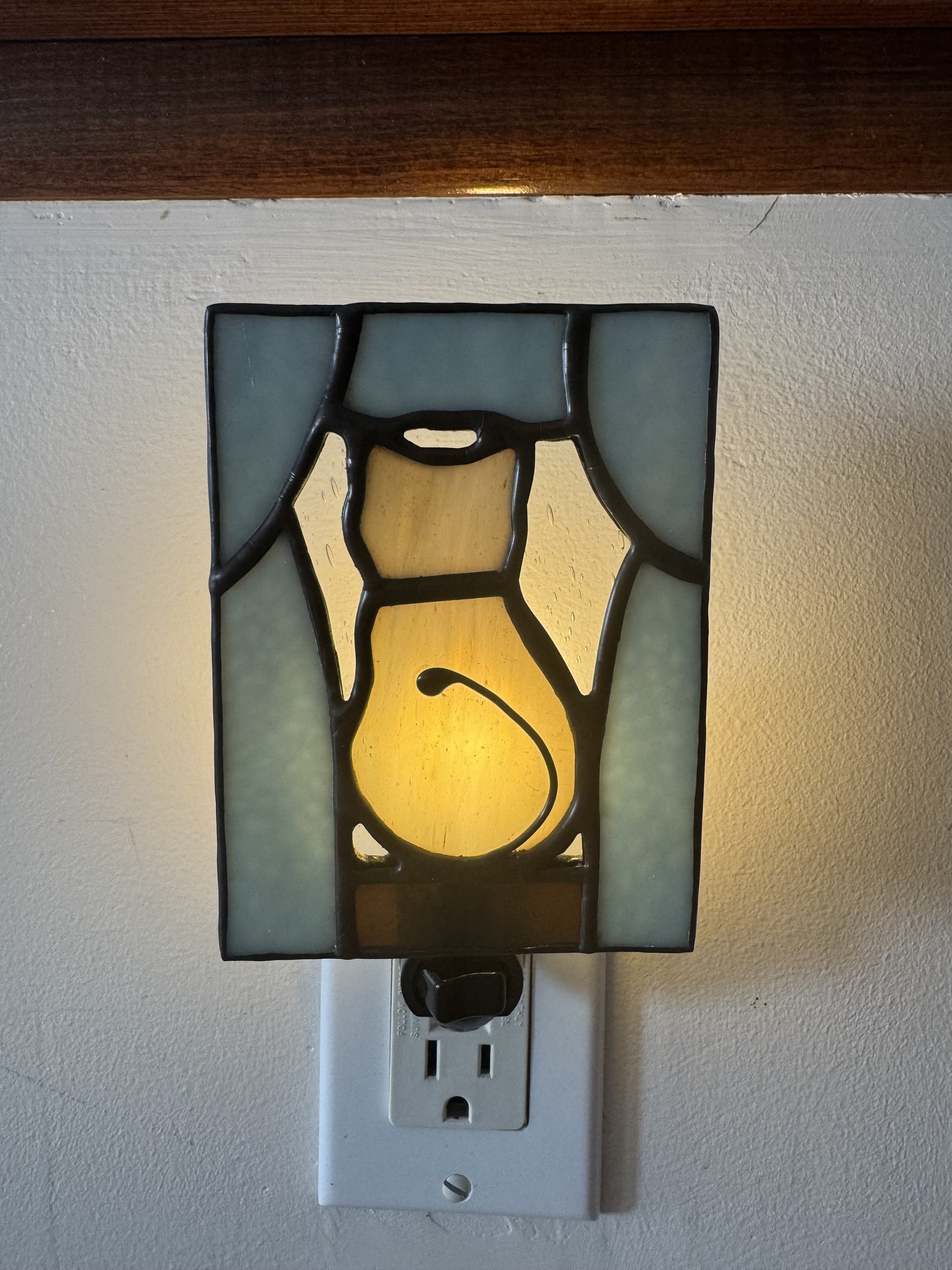 An electrical outlet with a stained glass decorative cover on a white wall.