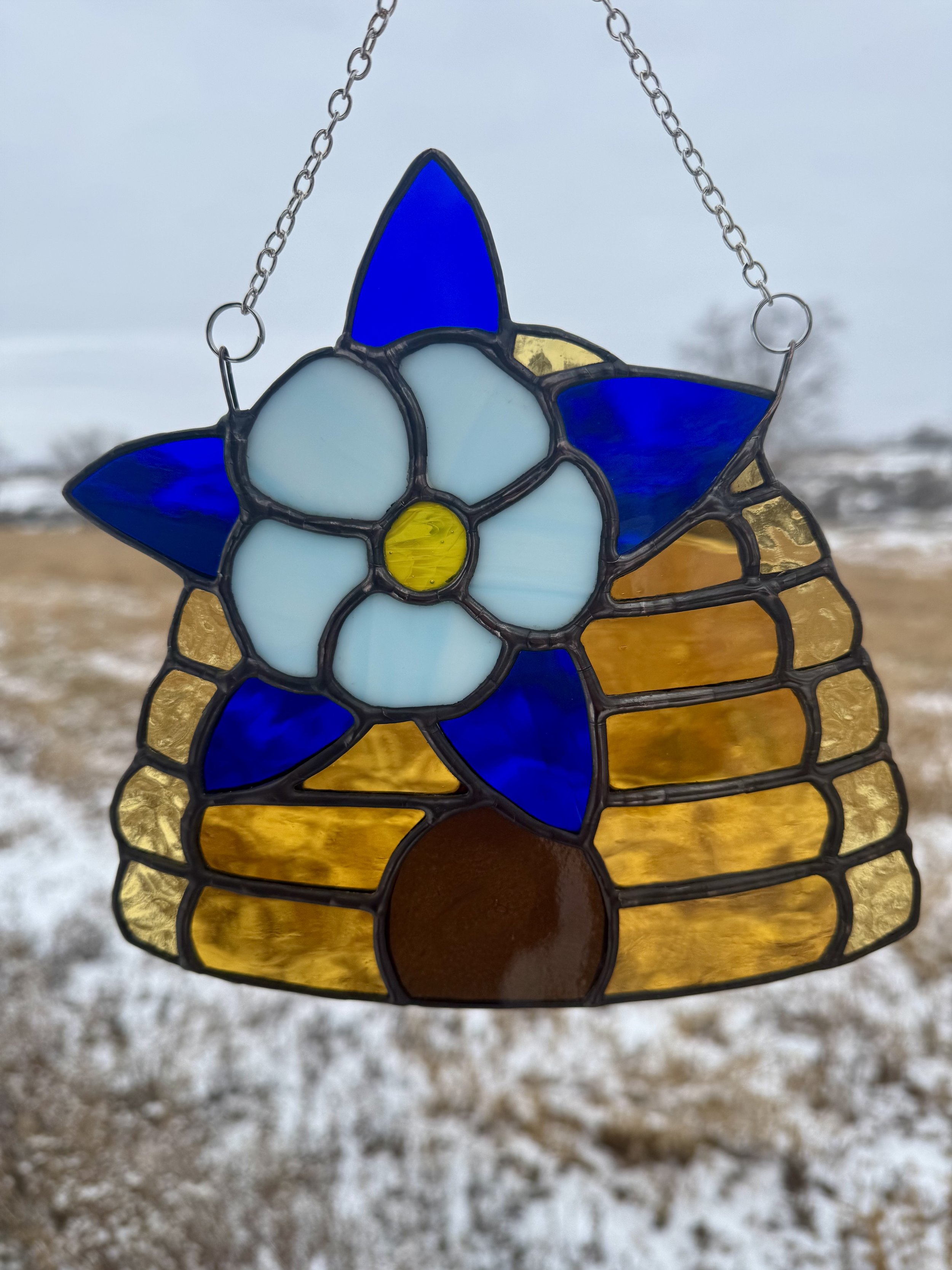 Close-up of a stained glass butterfly hanging outdoors with snowy ground and blurry trees in the background.