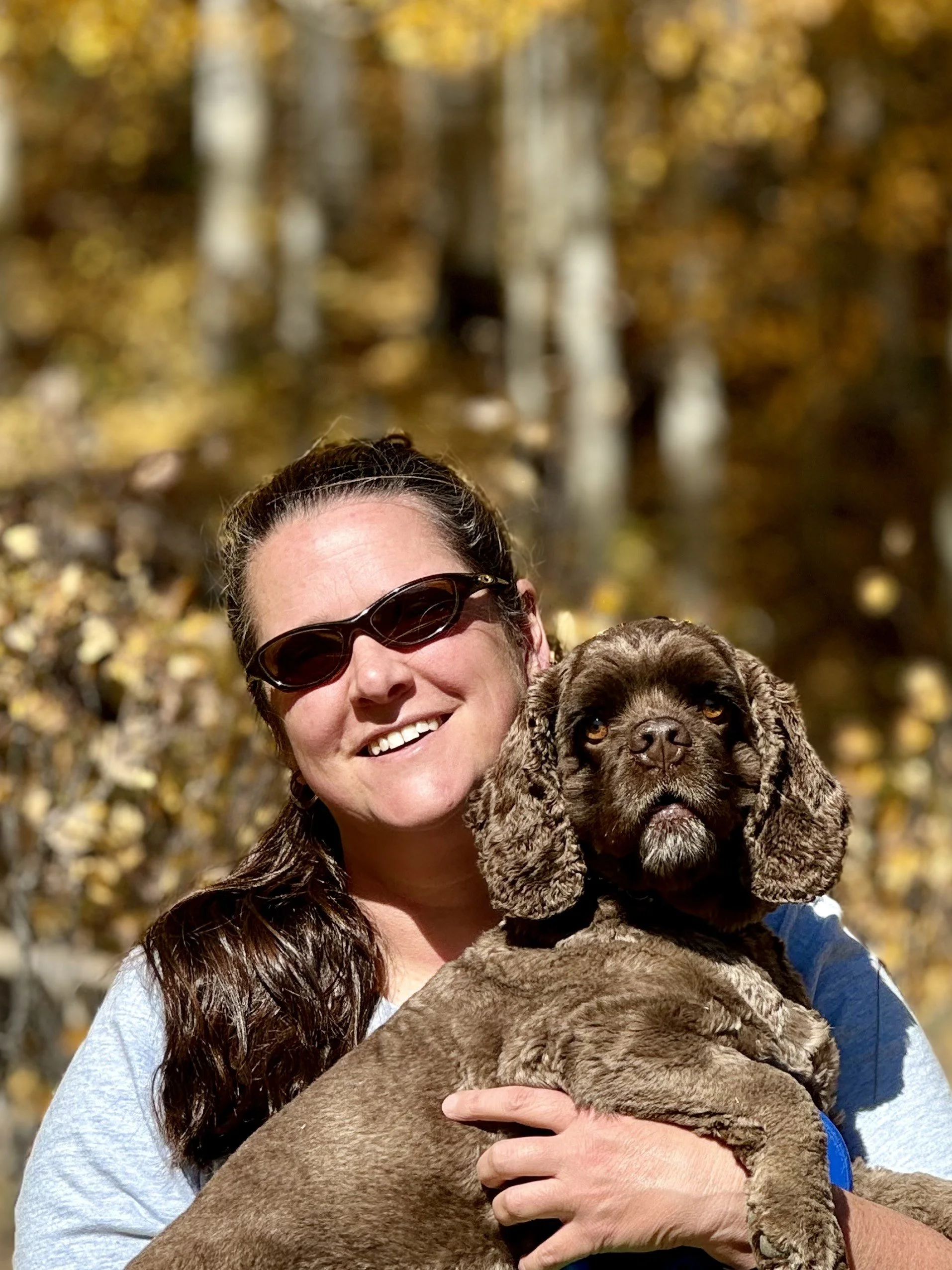 A woman holding a large brown puppy outside with autumn leaves in the background.