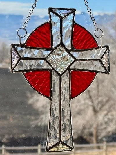 Stained glass cross with red circles in background, hanging outdoors.