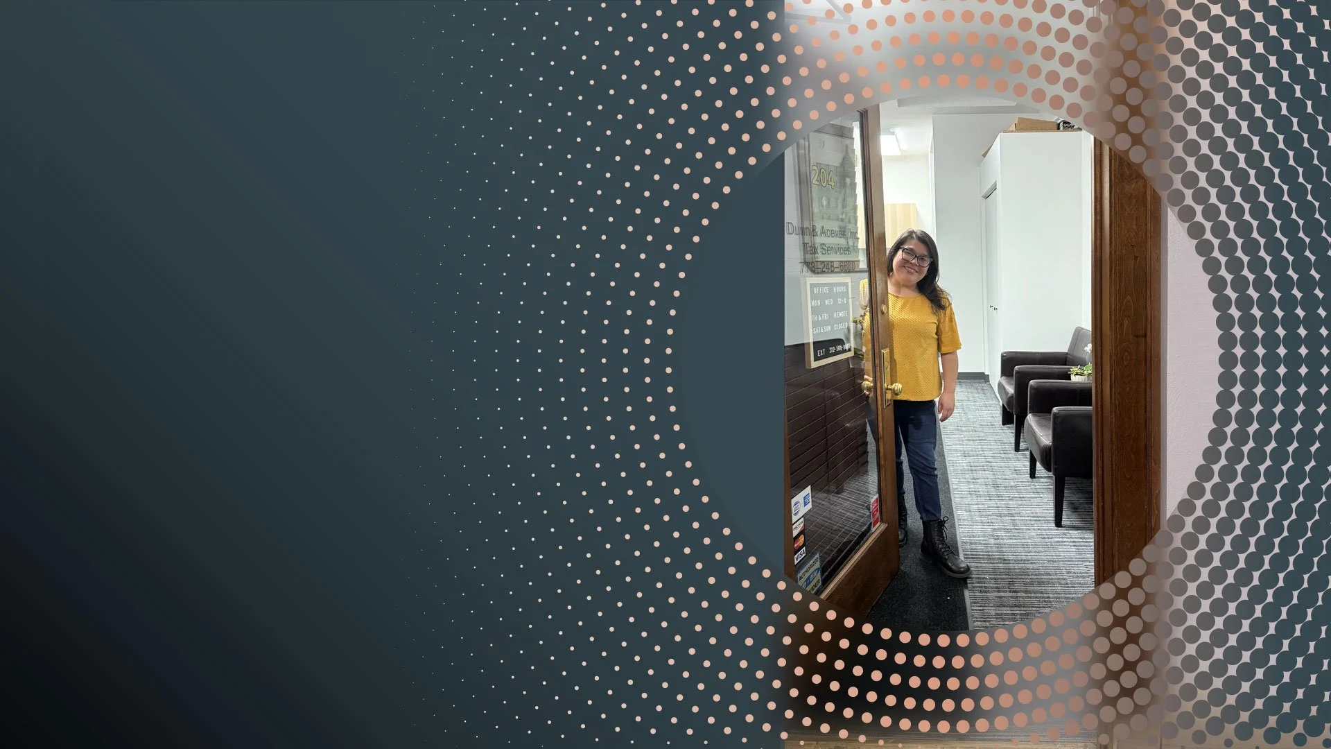 A woman with glasses, wearing a yellow top and dark pants, standing in a doorway inside an office or waiting room, smiling.