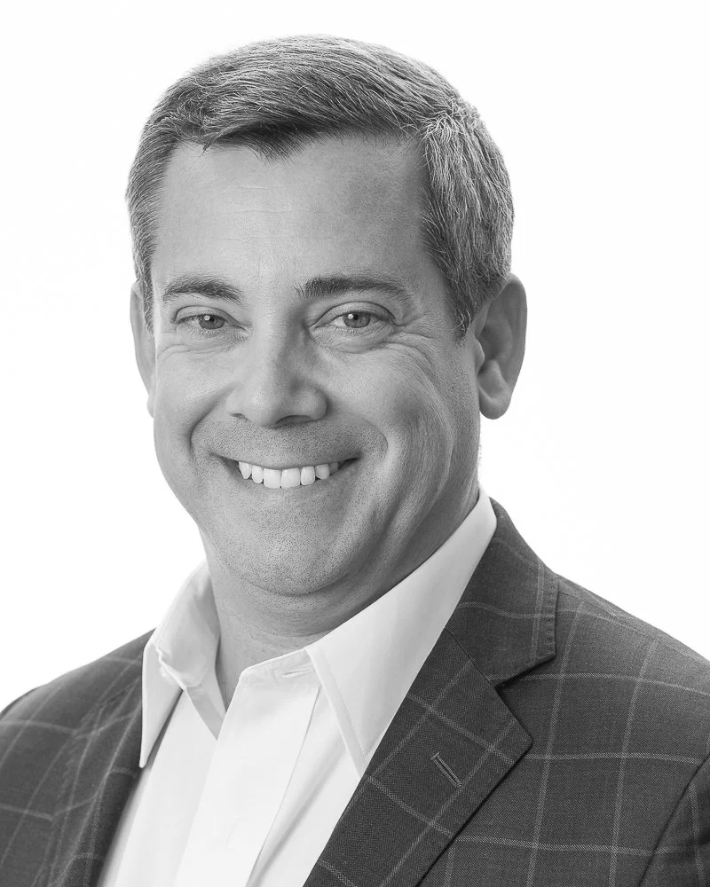 Black and white portrait of a smiling man in a checked blazer and white shirt.