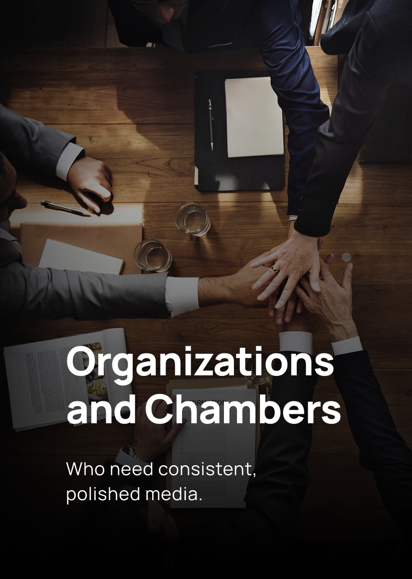 Top-down view of a wooden conference table with five business professionals placing hands together in a team cheer, with notebooks, glasses of water, and a pen on the table, displaying teamwork and collaboration.