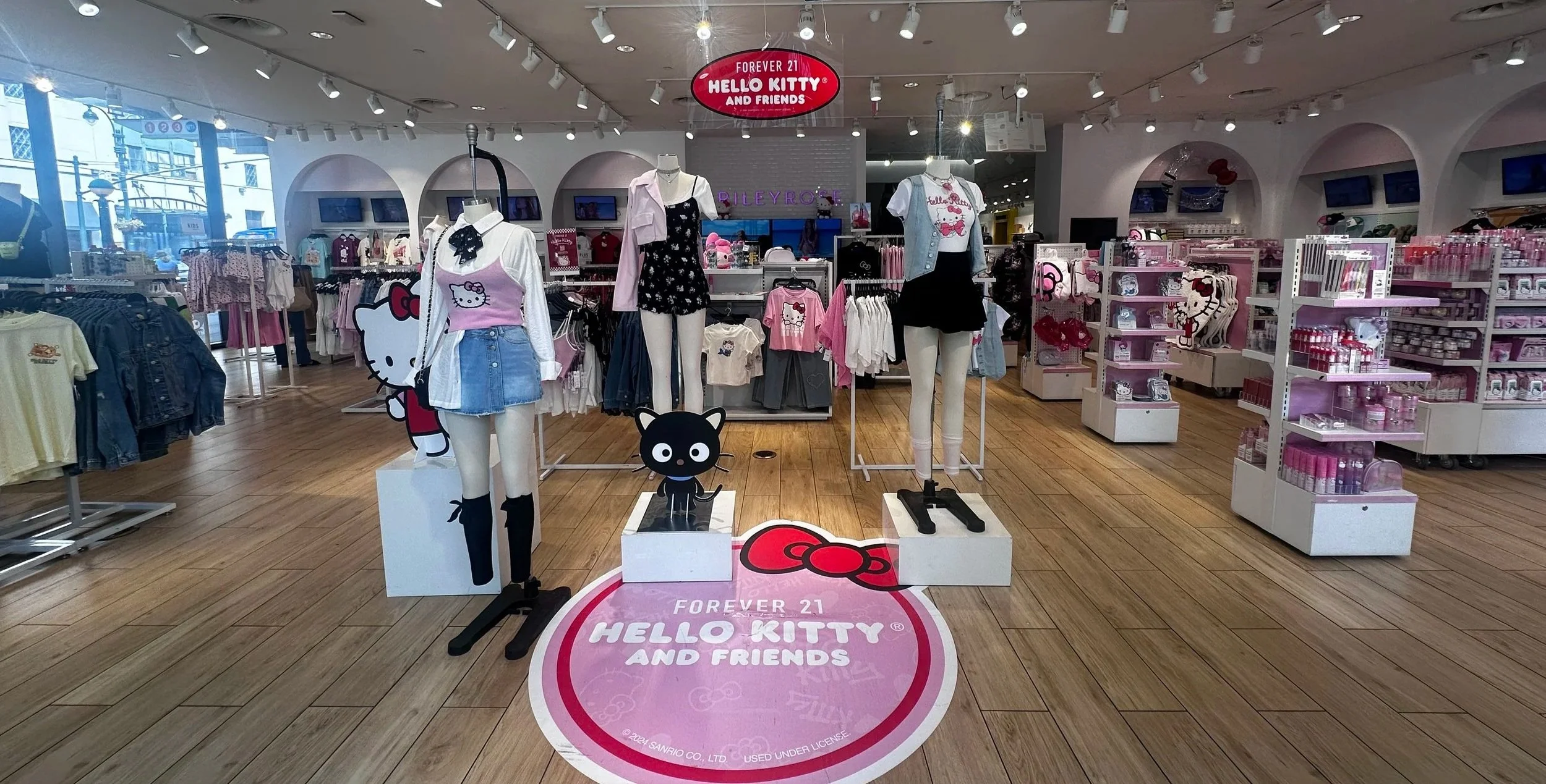 Hello Kitty themed display inside Forever 21 store with mannequins dressed in Hello Kitty merchandise, shelves filled with Hello Kitty products, and signage emphasizing the Hello Kitty branding.