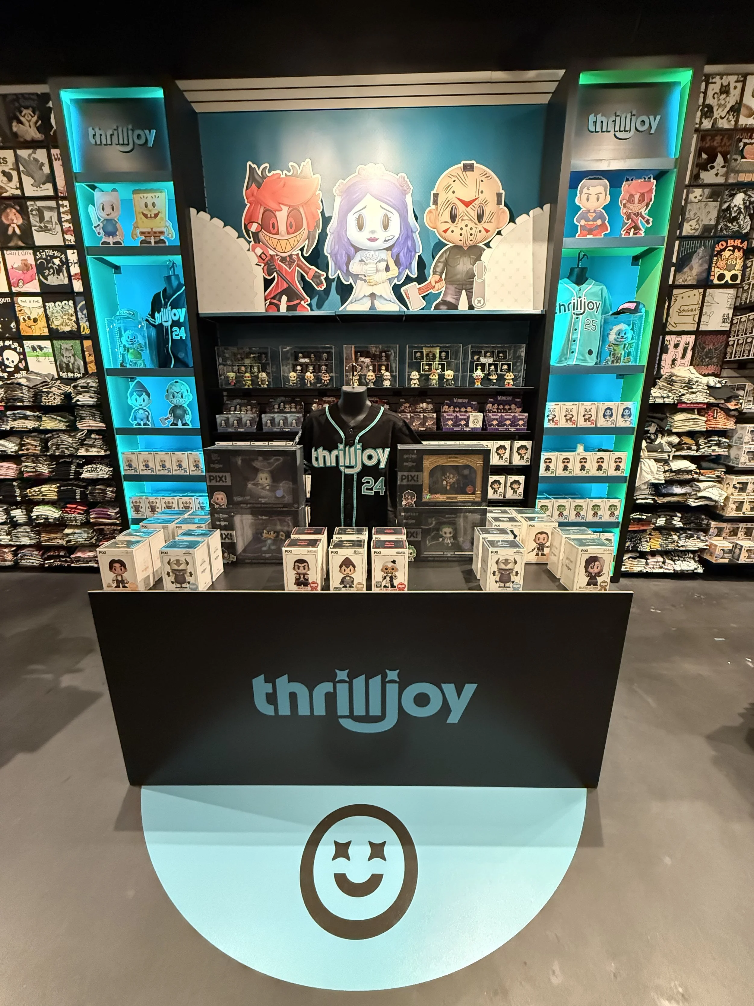 A retail display featuring horror and Halloween-themed Funko Pop! collectibles and merchandise from the brand Thrujoy, with character characters, clothing, and accessories arranged on illuminated shelves and a table with a mannequin. The backdrop has