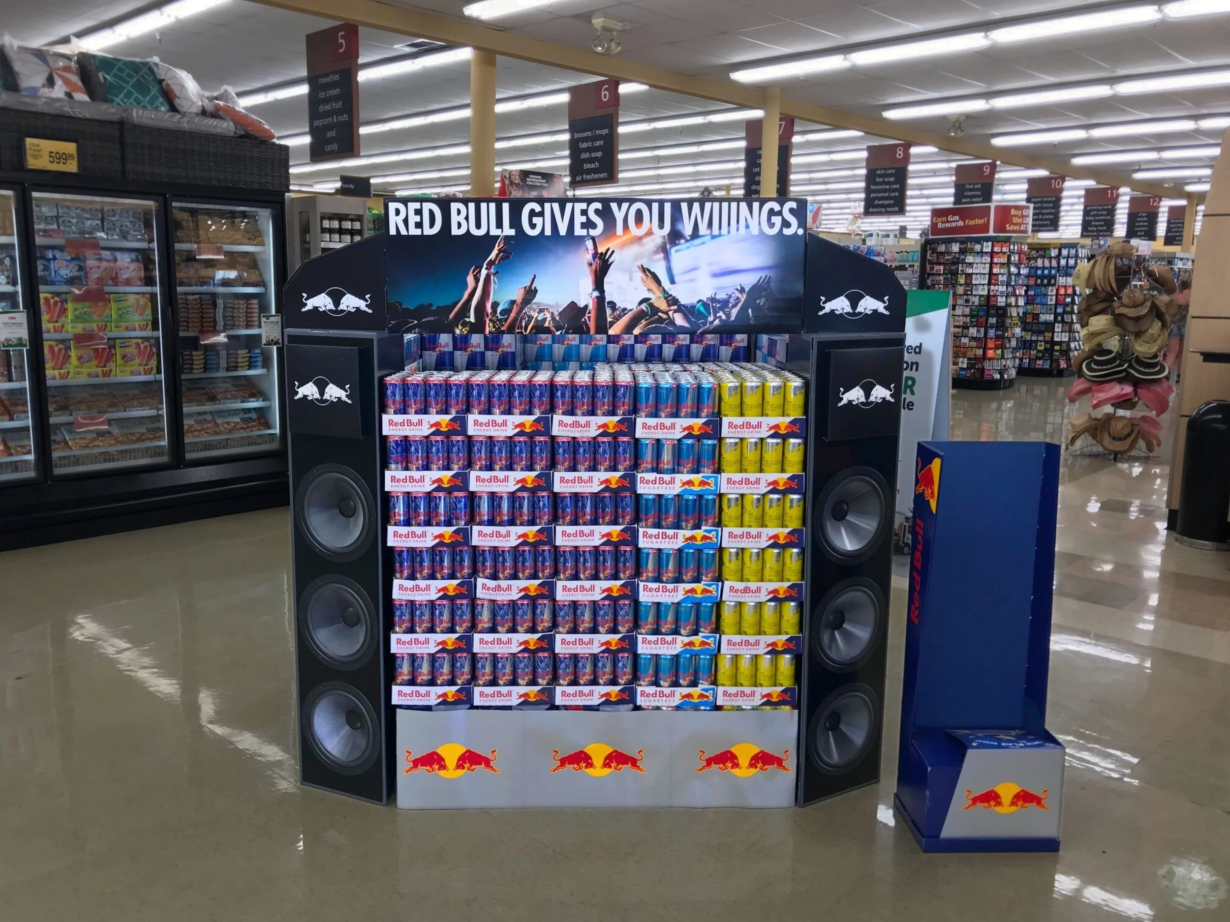 Display of Red Bull energy drinks in a retail store with a sign that reads "Red Bull gives you wings" and features two large Black Bull logos on either side.