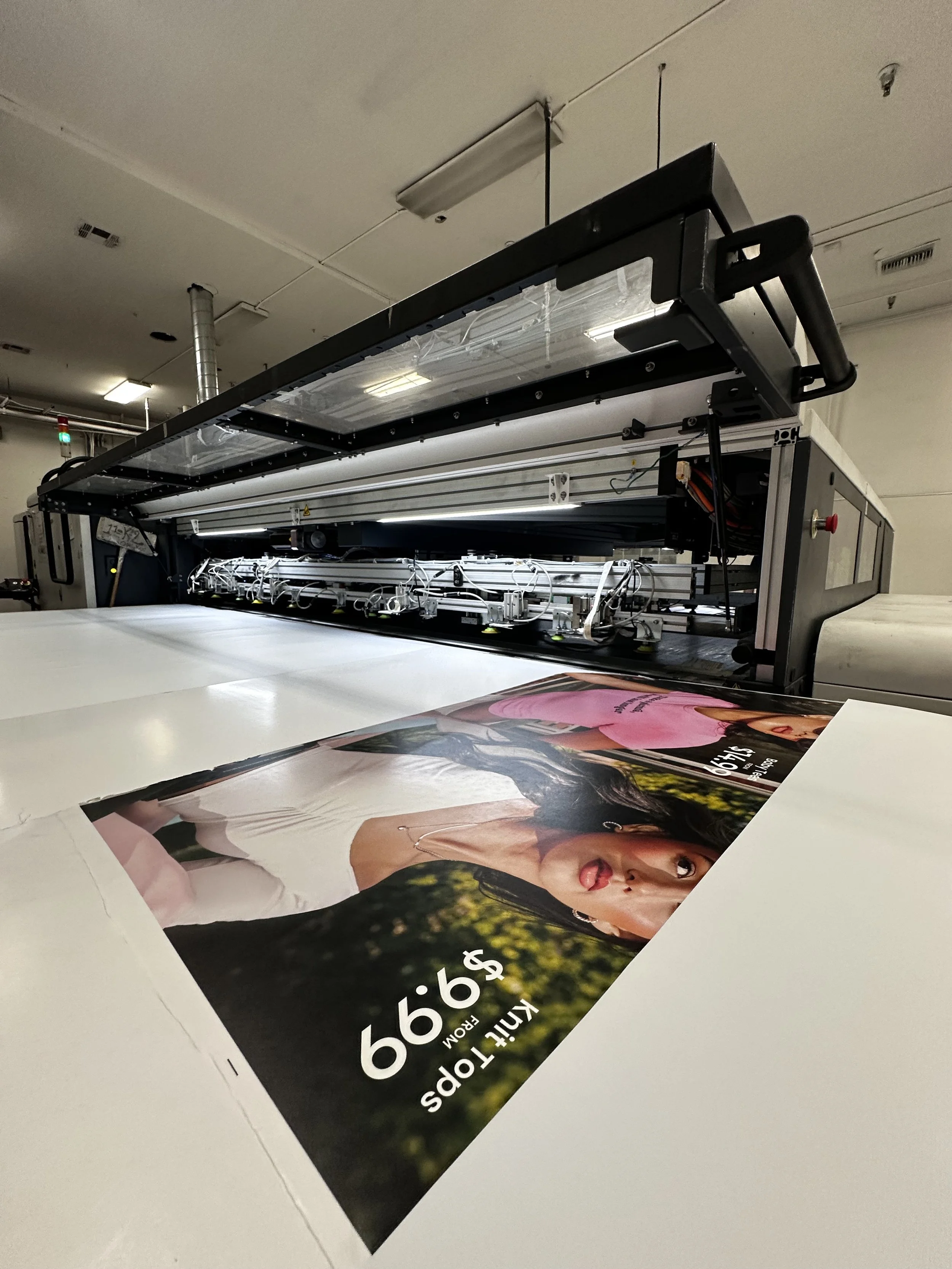 A large industrial printer printing a colorful advertisement featuring a woman making a playful face.