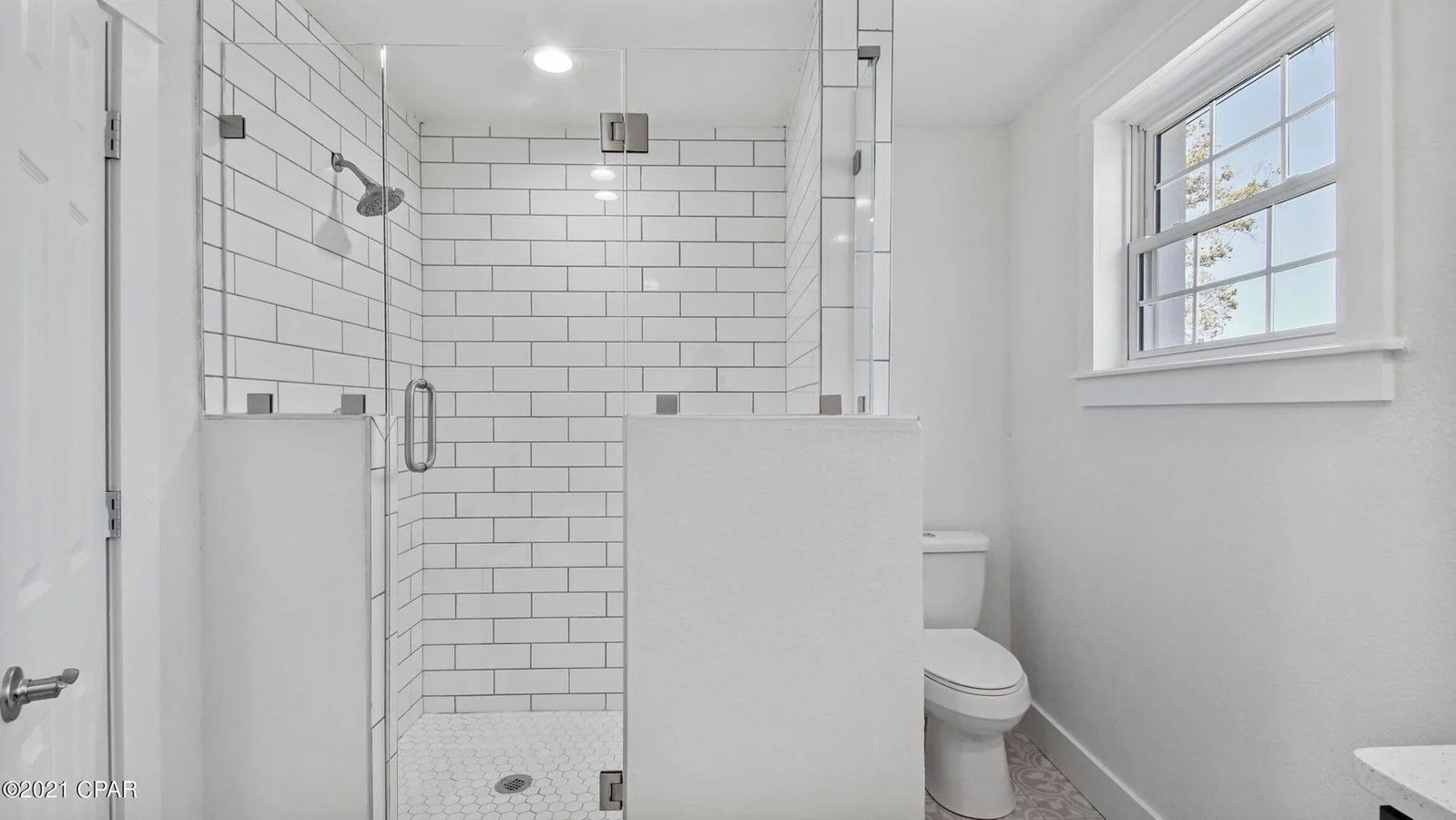 Modern bathroom with white subway tile shower, glass door, and a window with multiple panes.