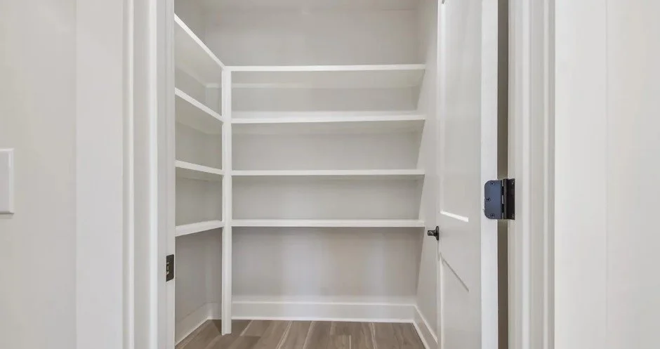Empty white built-in corner shelves in a small closet with a closed door.