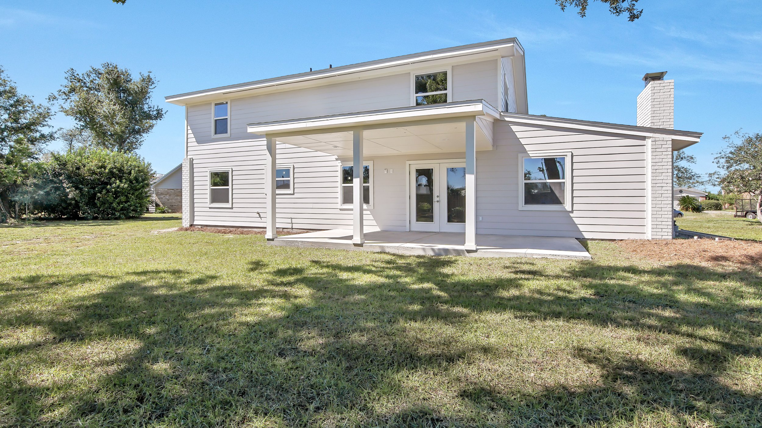 Front view of a modern white two-story house with a small covered porch, large backyard with grass, and trees in the background.