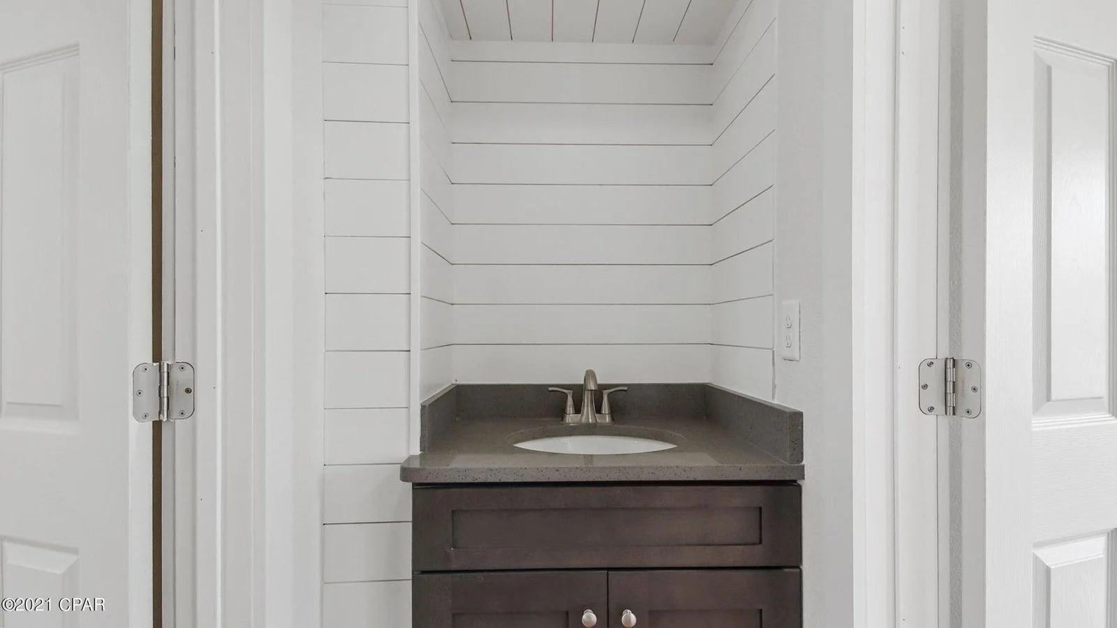 Bathroom vanity with a sink and faucet, surrounded by white paneled walls and partially open white doors.