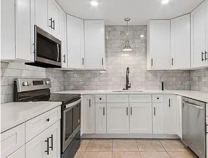 Kitchen with white cabinets, stainless steel appliances, gray subway tile backsplash, and tile flooring.